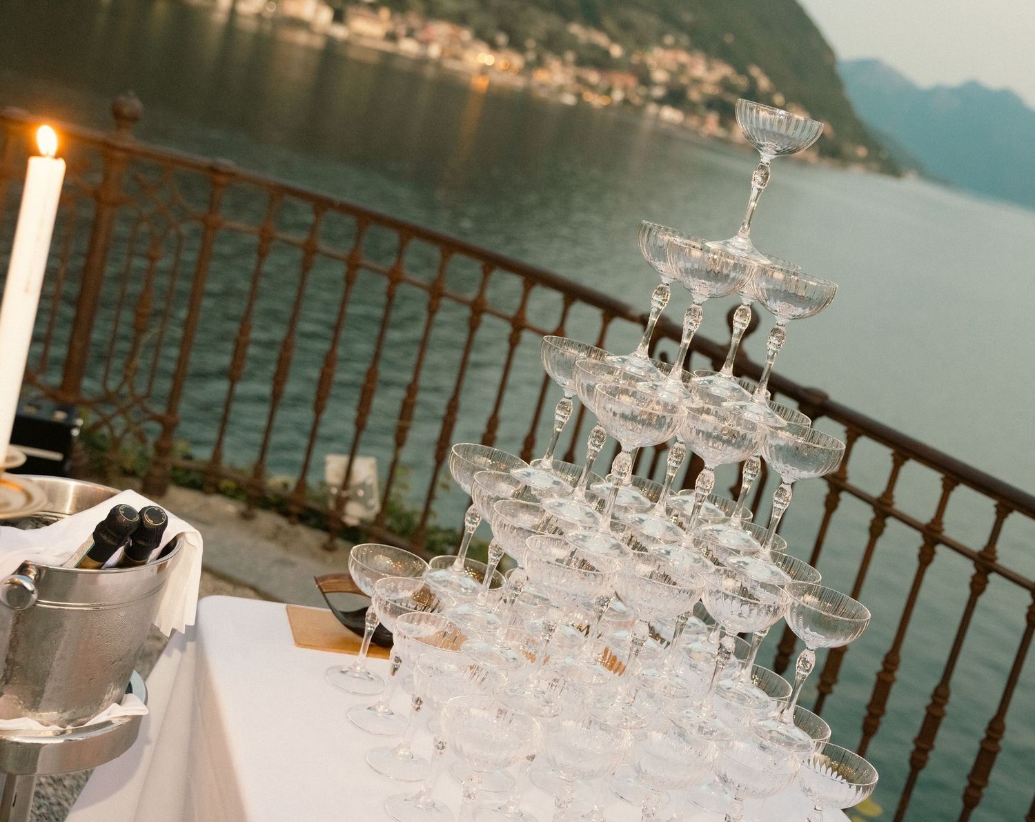 Empty wine glasses arranged in rows on an outdoor terrace overlooking a scenic mountain lake view.