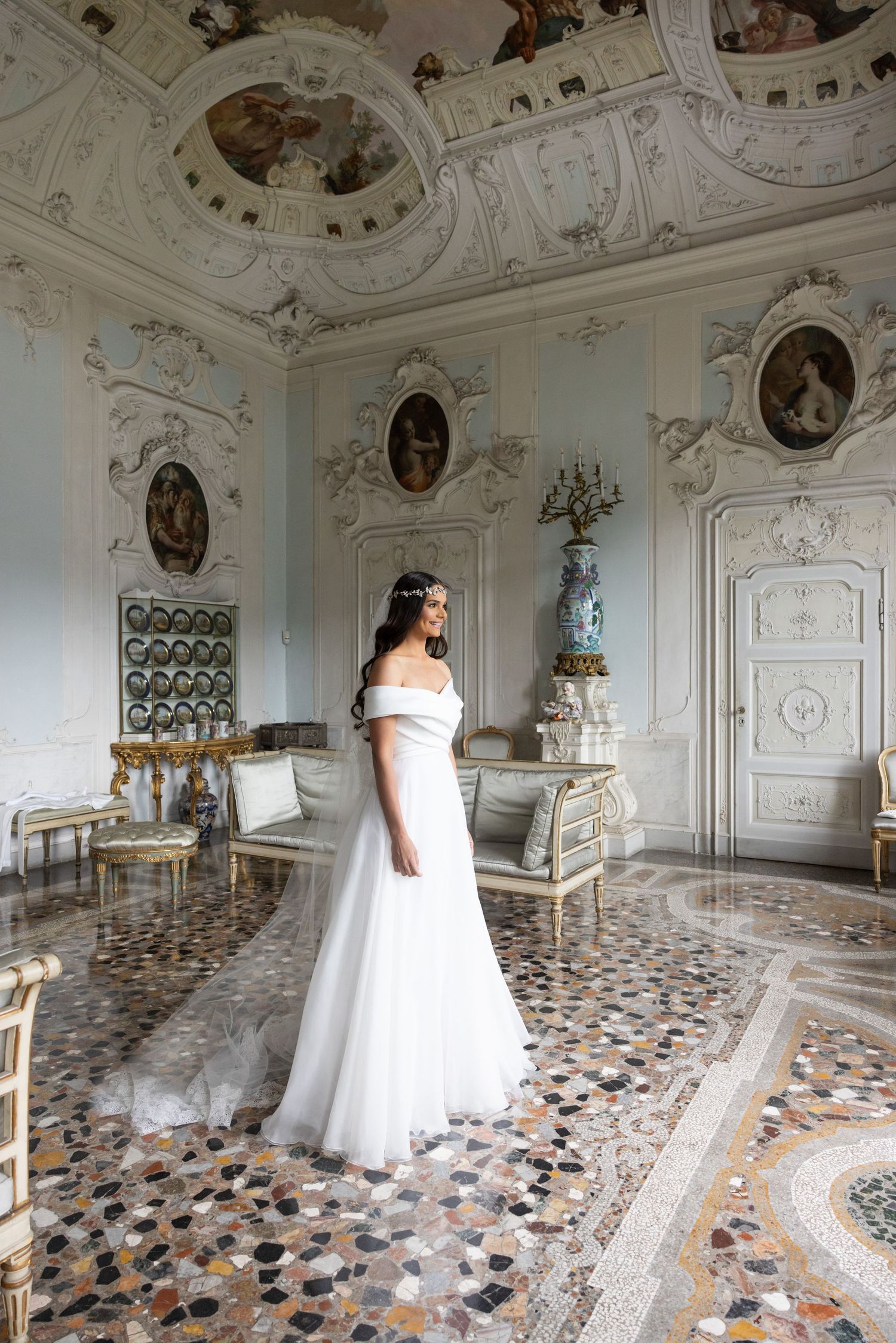 Bridal gown displayed in ornate Italian villa room with frescoed ceiling and marble floors.