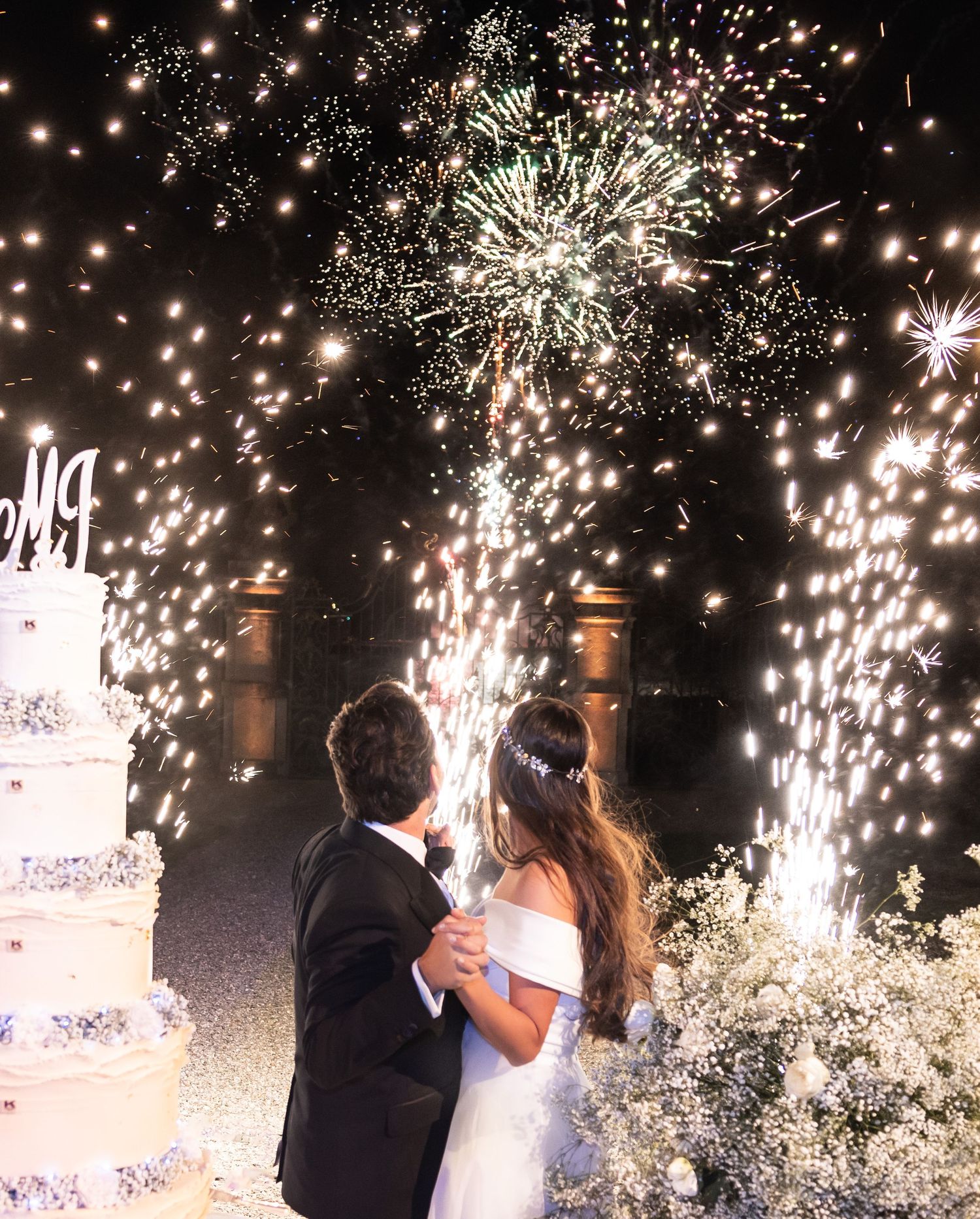 Dramatic sparkler display illuminates a wedding reception at night with a white cake.