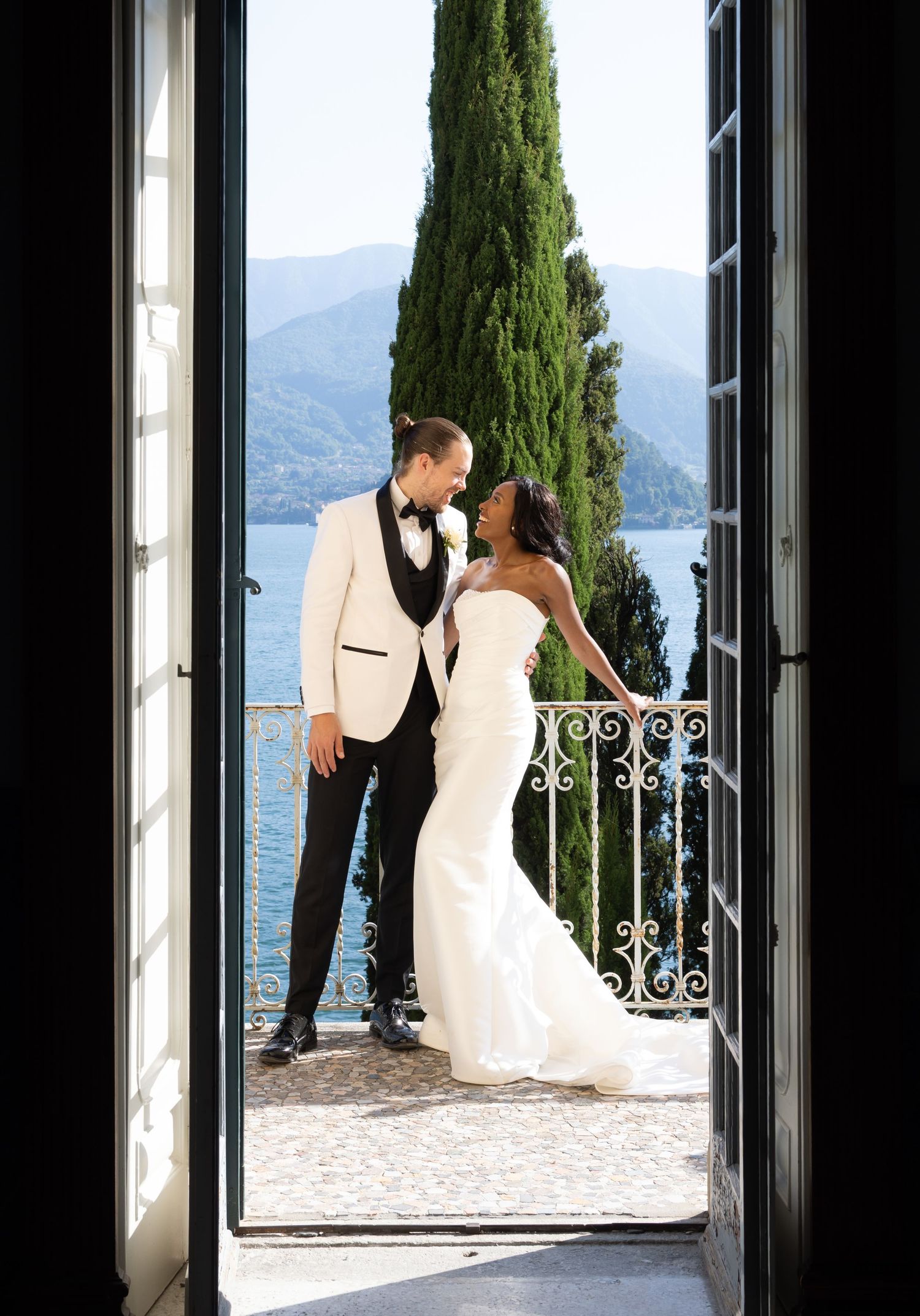 A couple in wedding attire shares a romantic moment on a terrace overlooking Lake Como in Italy.