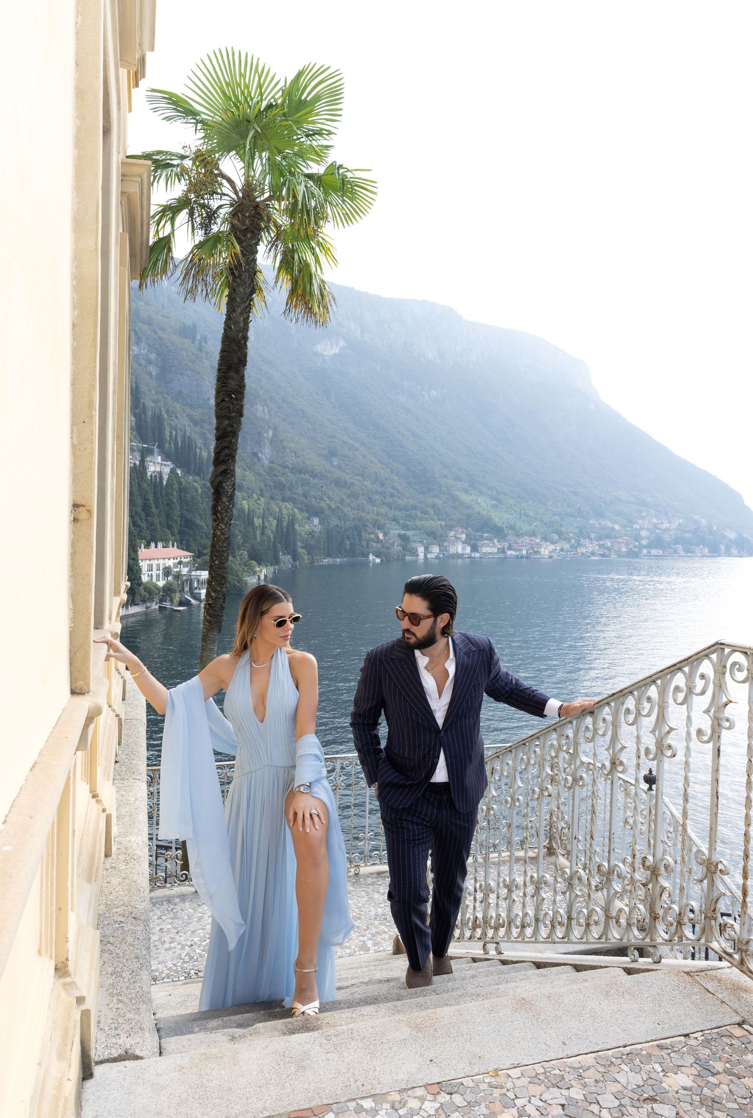 Elegant couple walking up ornate stairs by Lake Como with palm tree and mountain vista in Italy.
in the Villa Cipressi on Lake Como