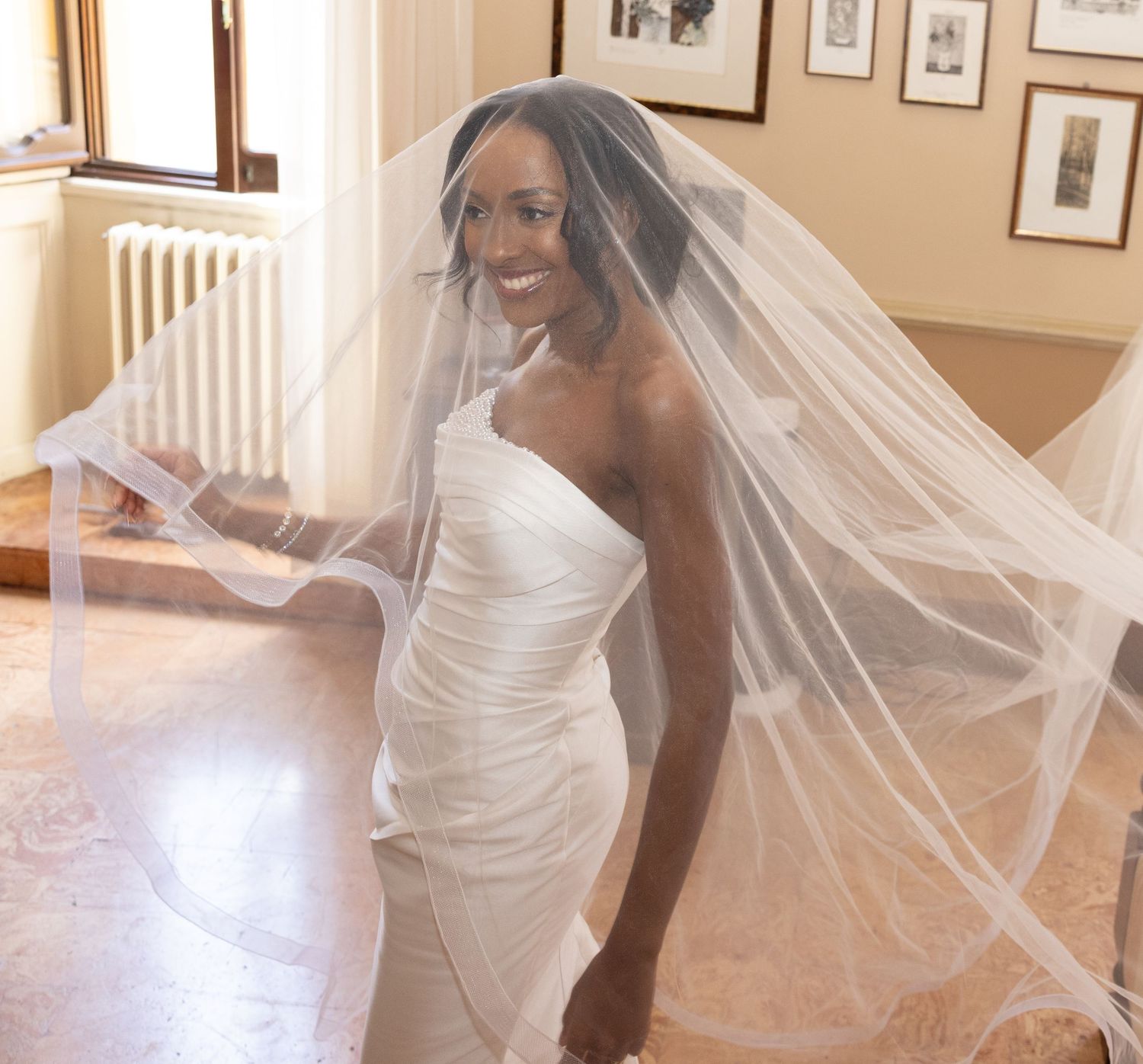 A bride in a white wedding dress twirls and dances, creating a flowing movement with her long veil in an elegant room.