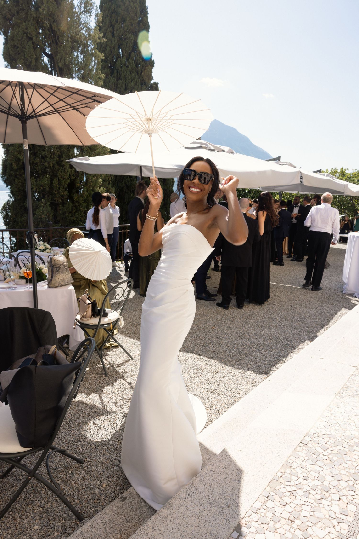 A row of white parasols line an outdoor event space where guests gather on a sunny day.