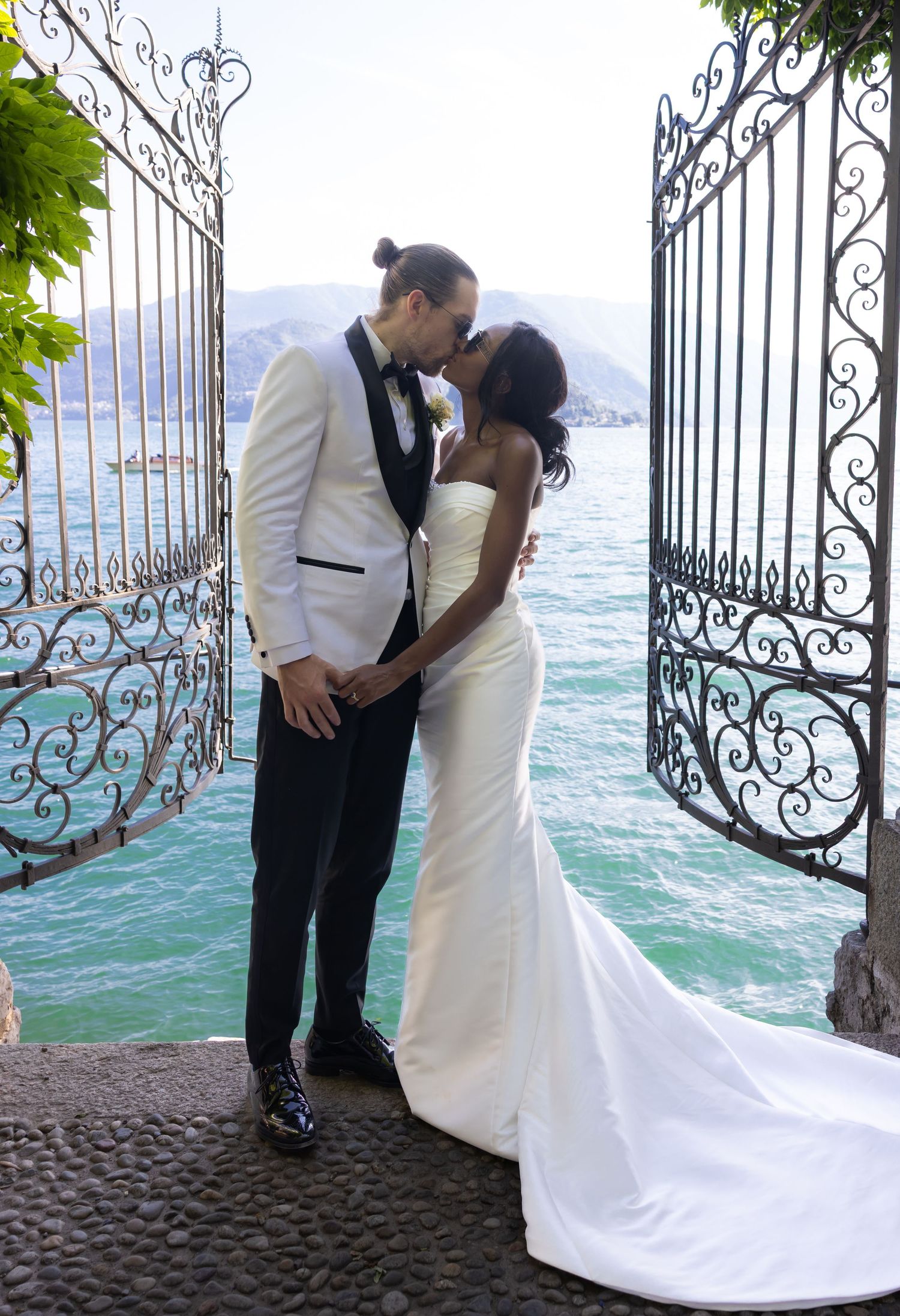 A romantic wedding couple shares intimate kisses against an ornate iron gate with ocean waves in the background.