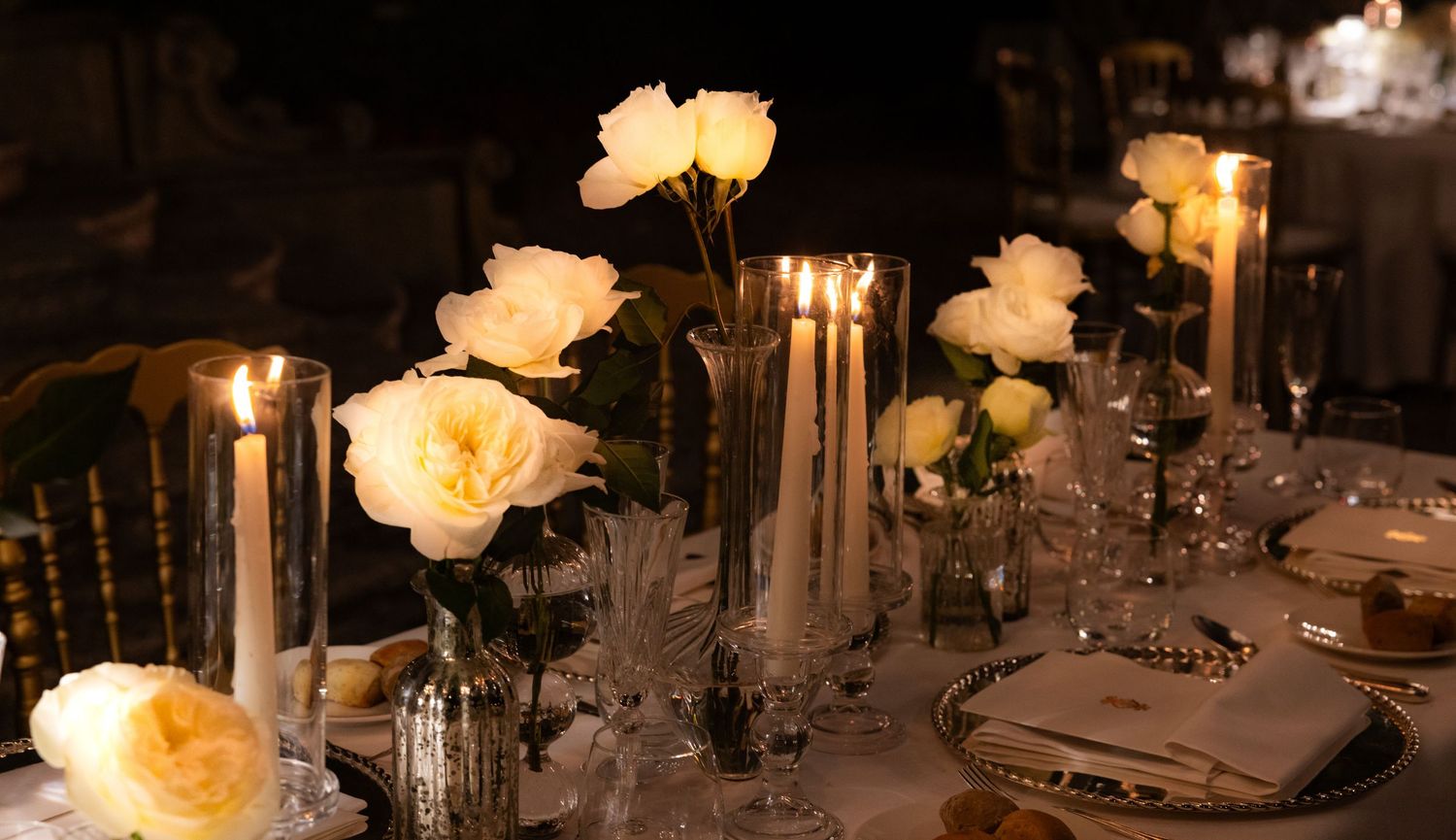 Romantic table settings with soft lighting and cream-colored roses in glass vases.