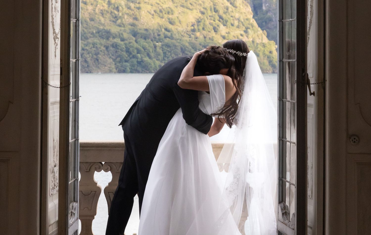 Couple in wedding attire silhouetted against bright doorway in romantic moment.