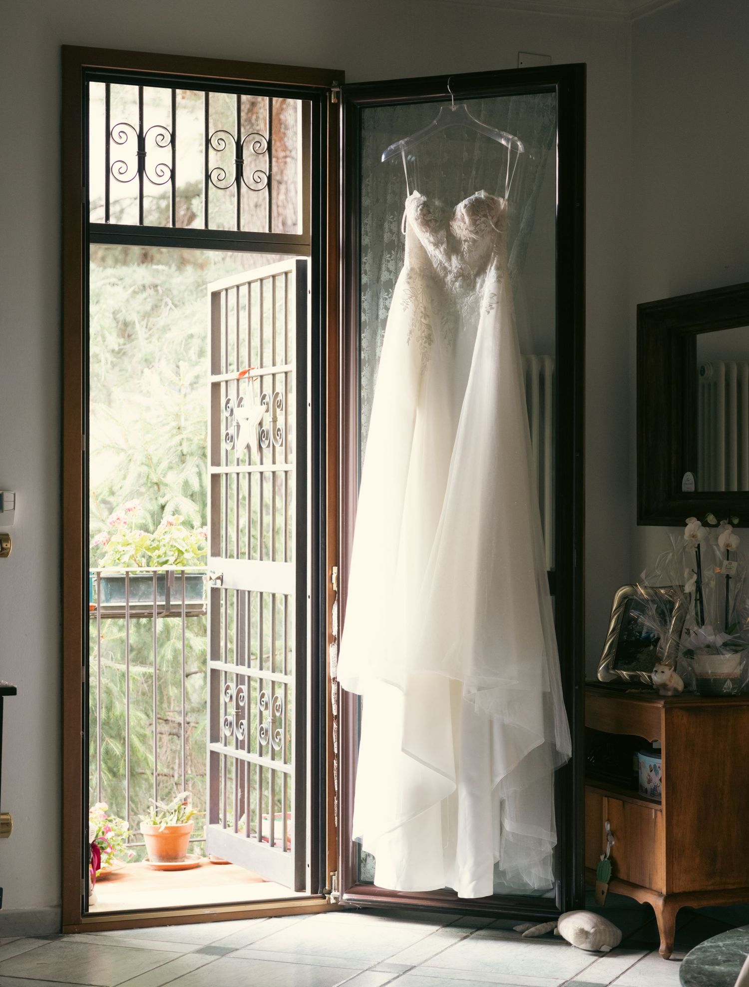 White wedding dress hanging by window with natural light streaming in.