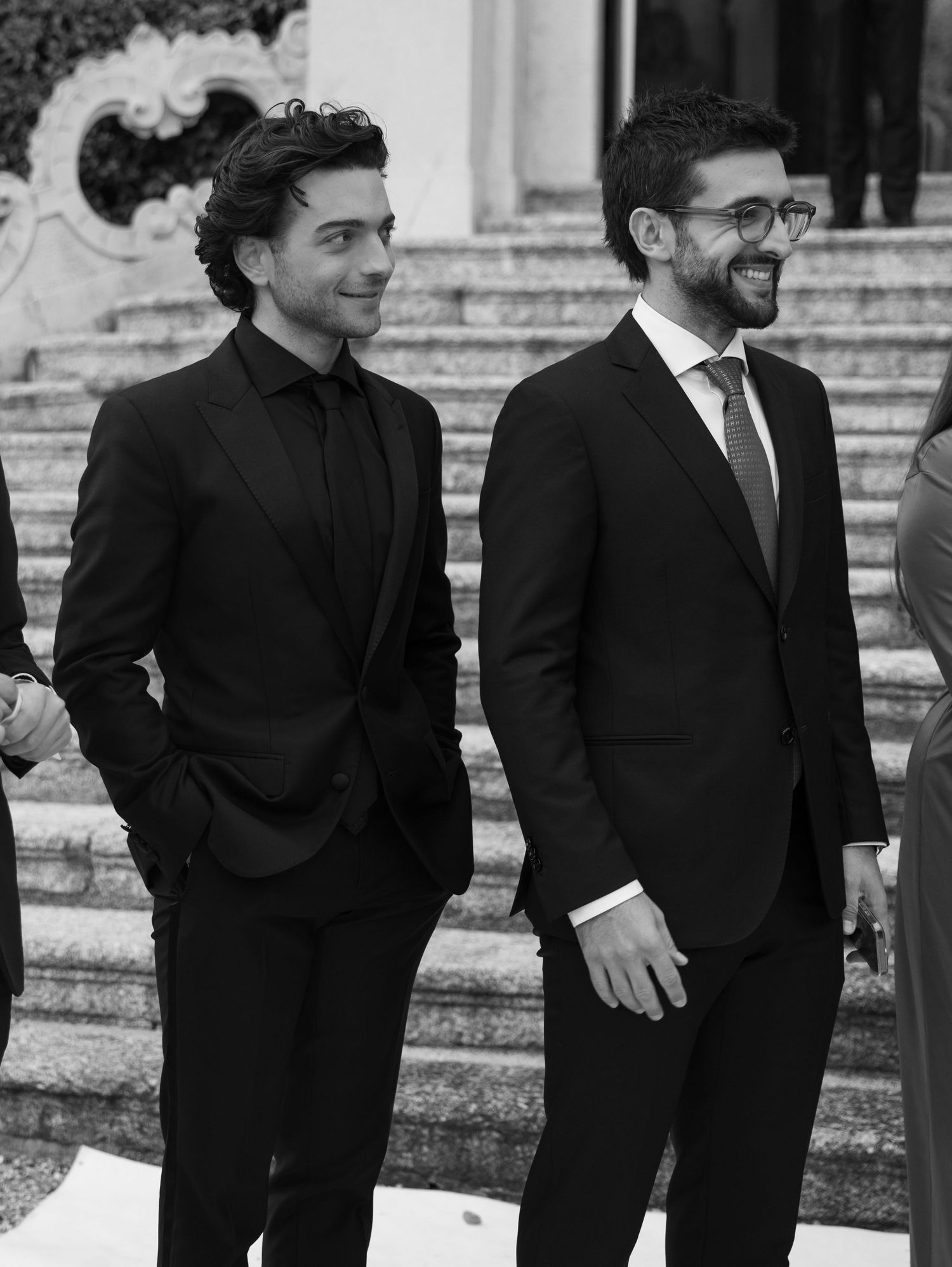 Groomsmen in black suits posing on stone steps of historic building.