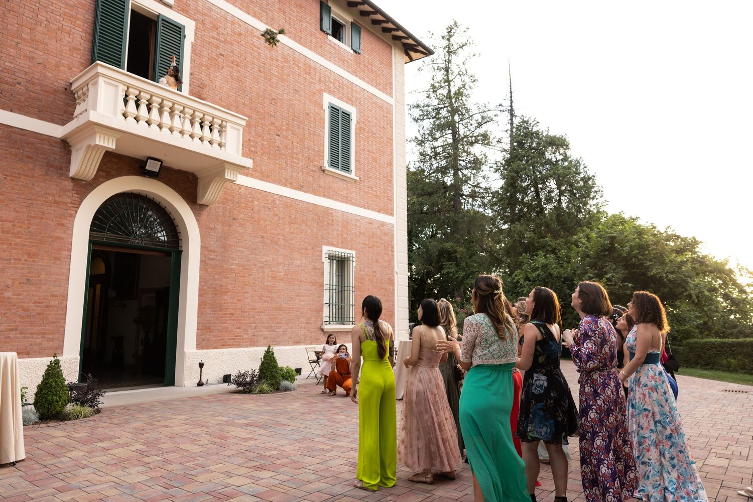 Wedding guests gathering outside a brick building with arched doorways.