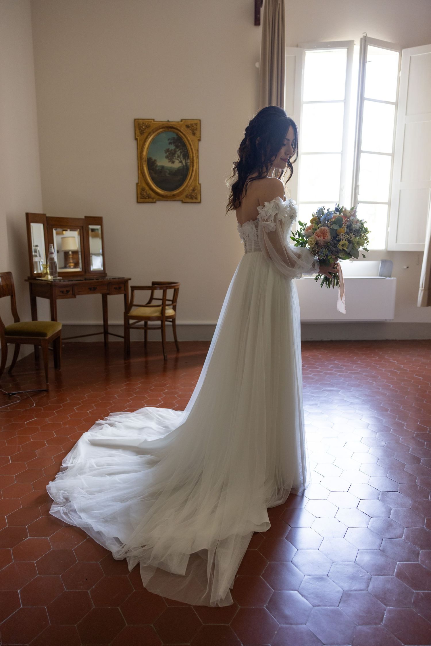 Flowing white wedding dress train sweeps across terracotta tile floor in elegant room.
