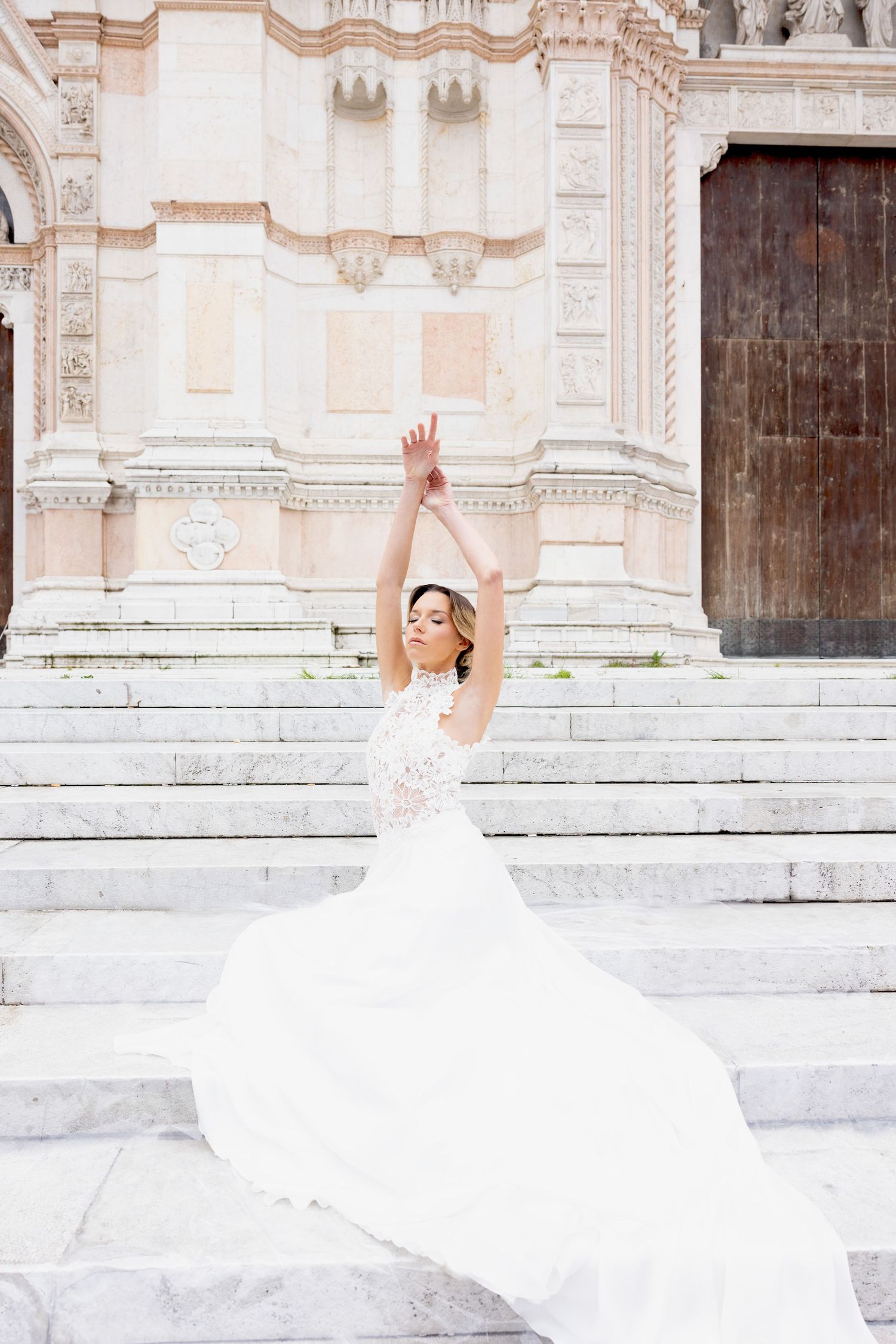 Flowing white wedding dress captured in motion against ornate stone church steps.