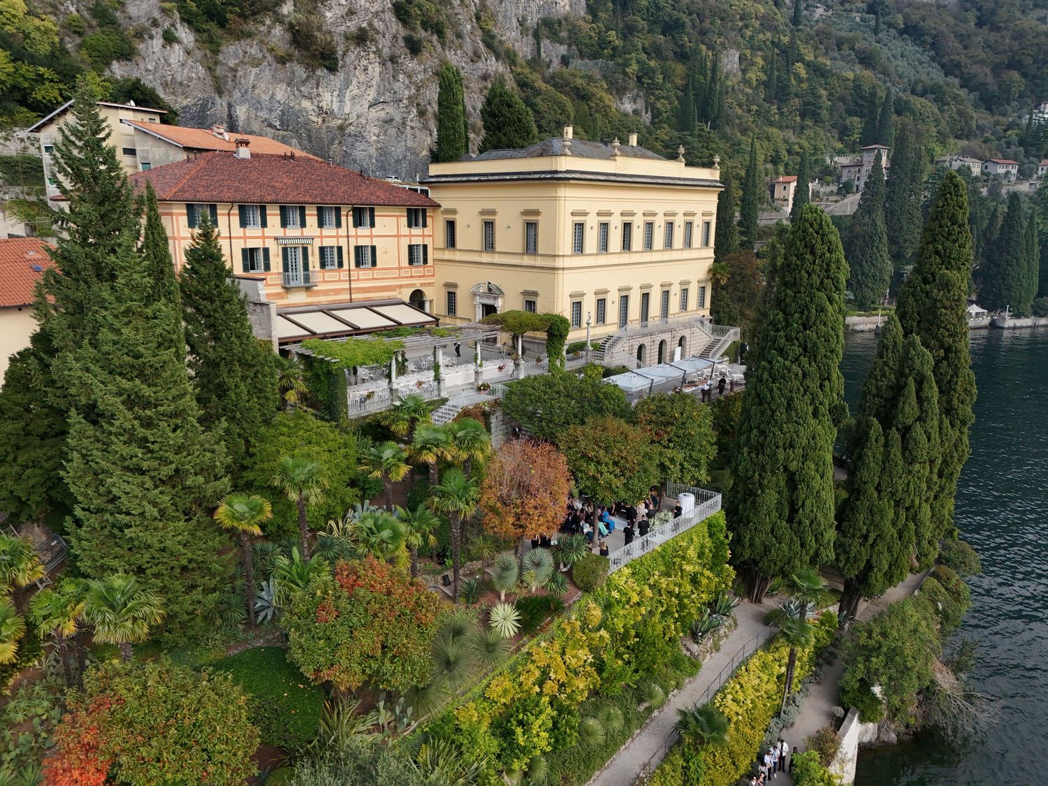 Scenic aerial view of Lake Como's shoreline with historic villas and lush gardens nestled against mountainous cliffs in Italy.