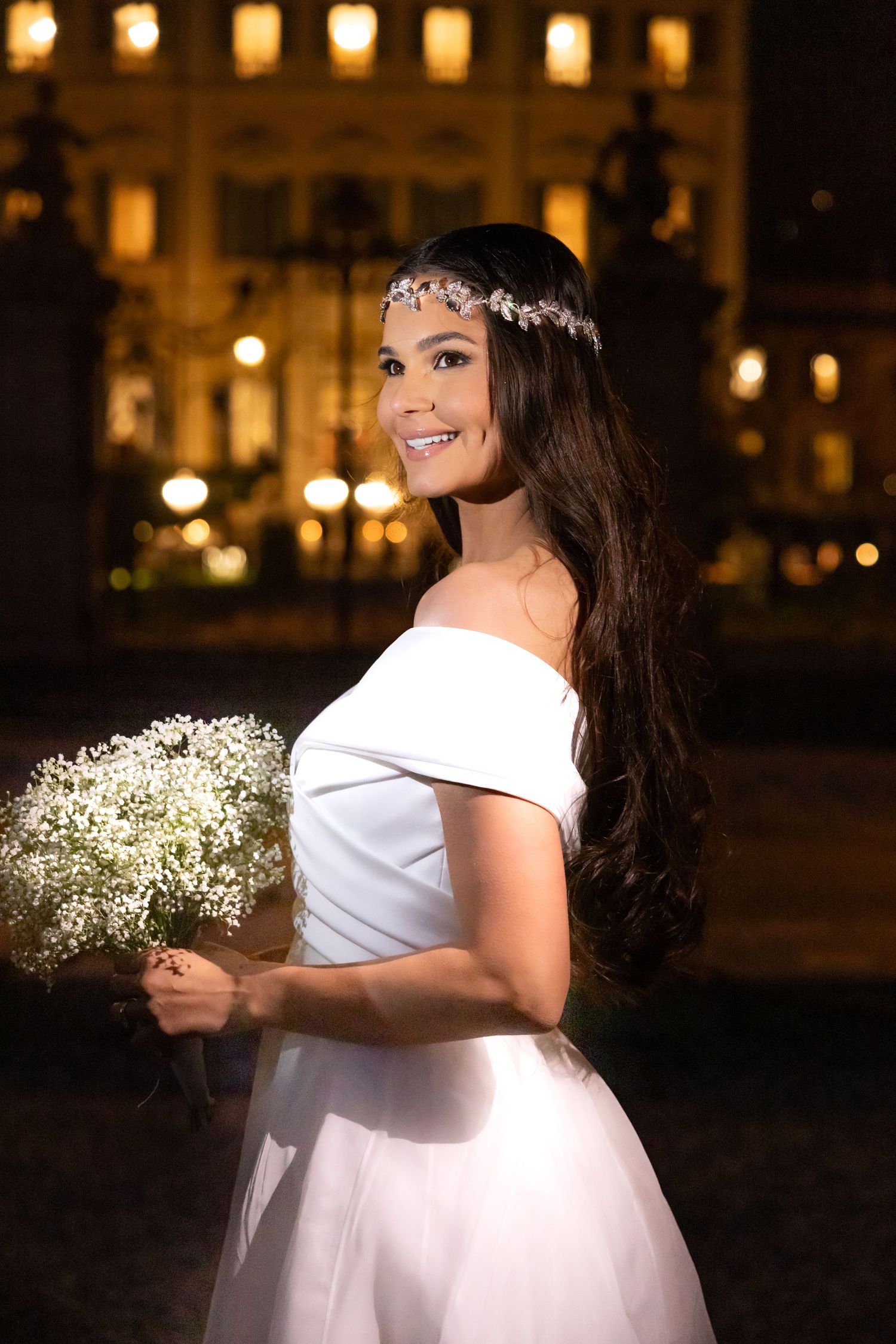 A bride holds a bouquet of baby's breath flowers in a warmly lit evening setting.