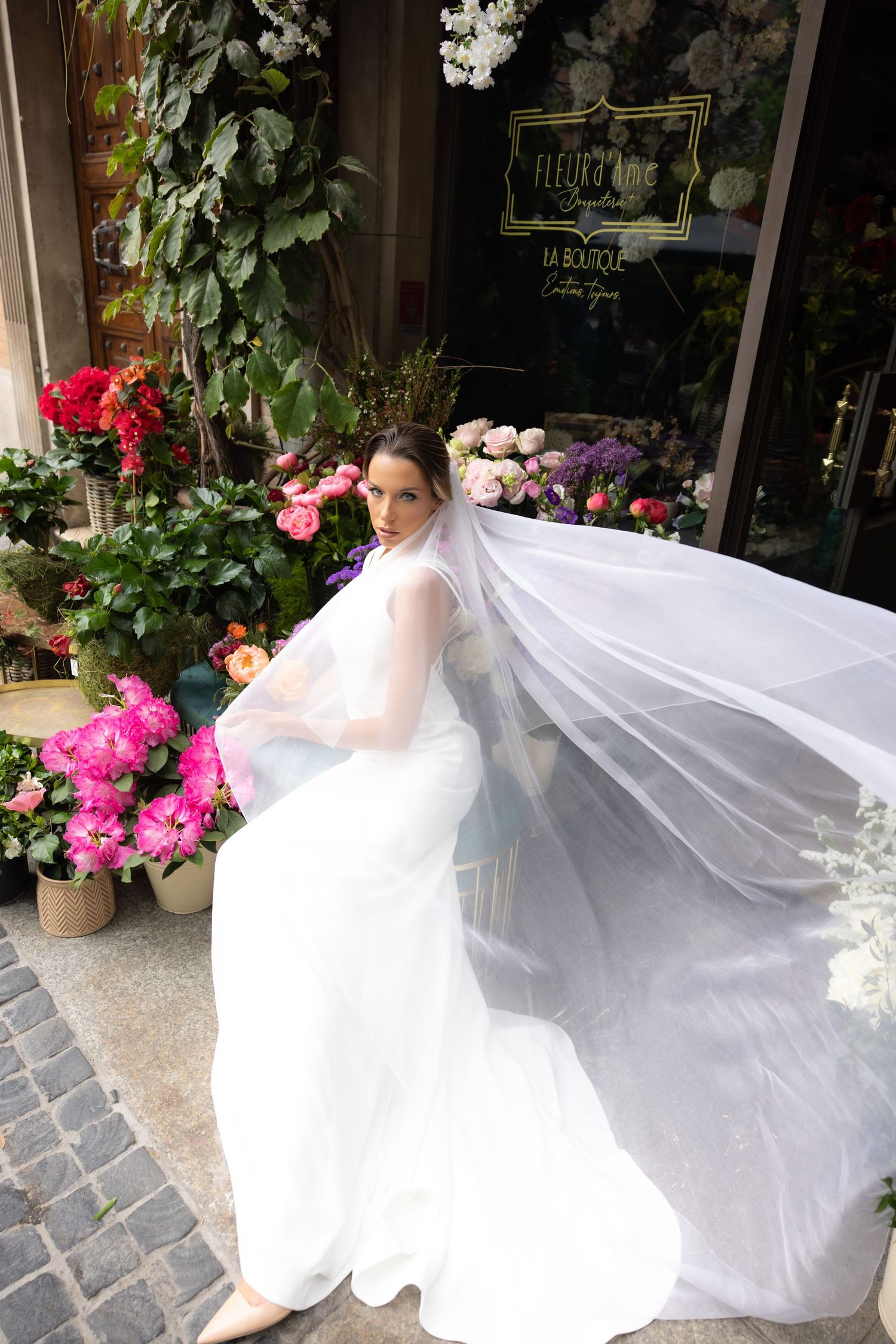 Flowing white wedding dress captured in motion against floral shop backdrop.