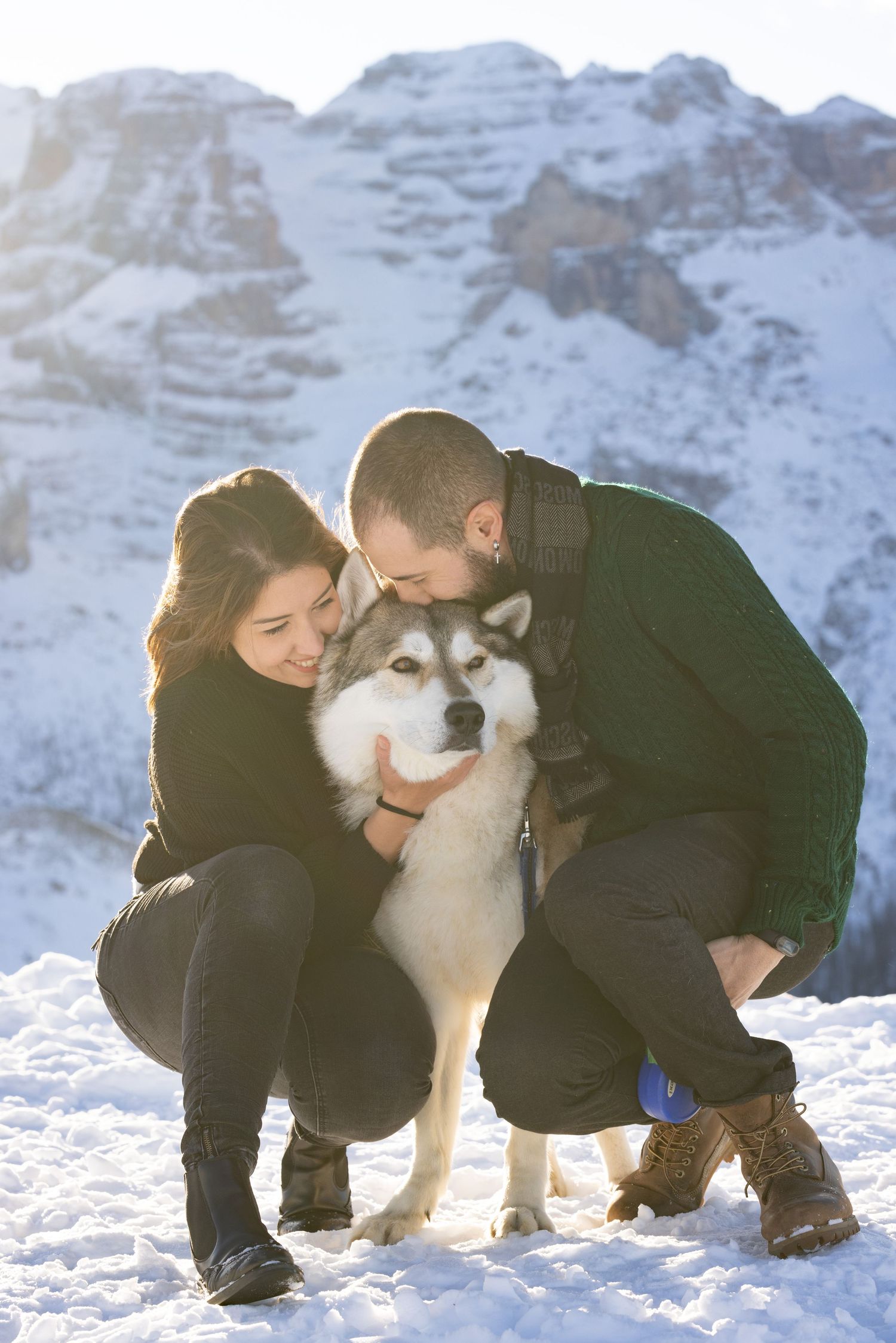A majestic Husky dog poses with its owners in a snowy mountain landscape.