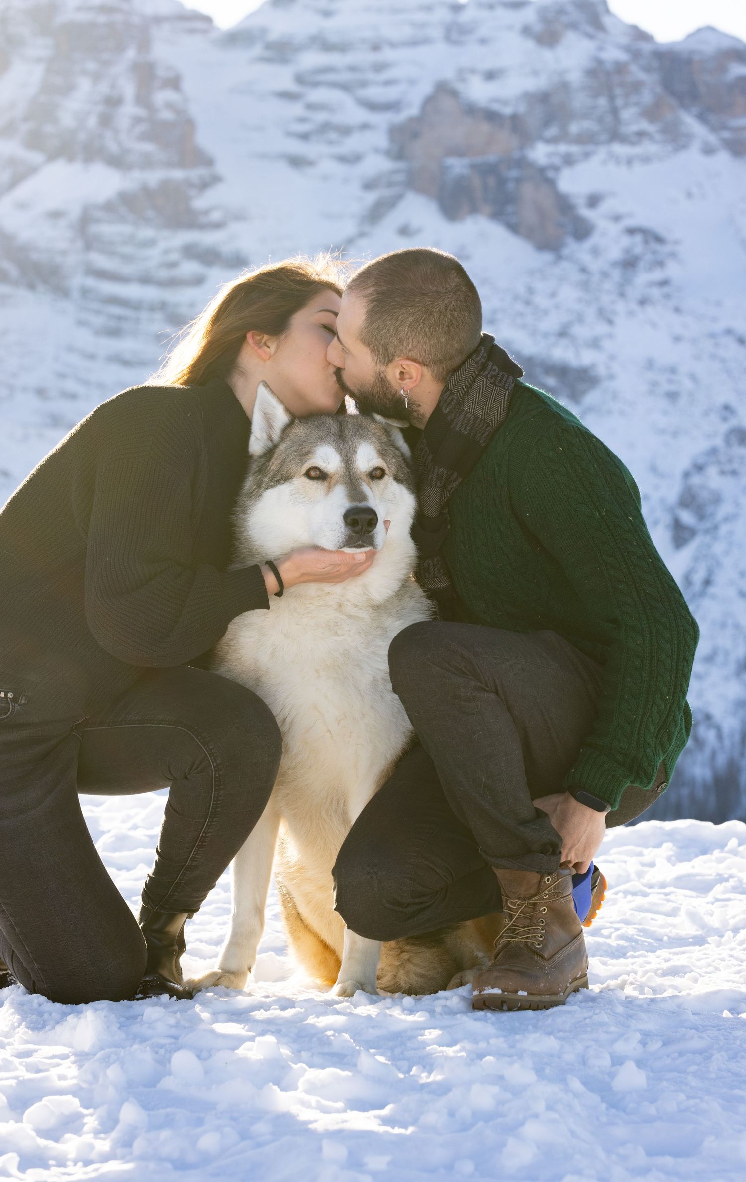 Malamute dog poses with couple in snowy mountain setting.