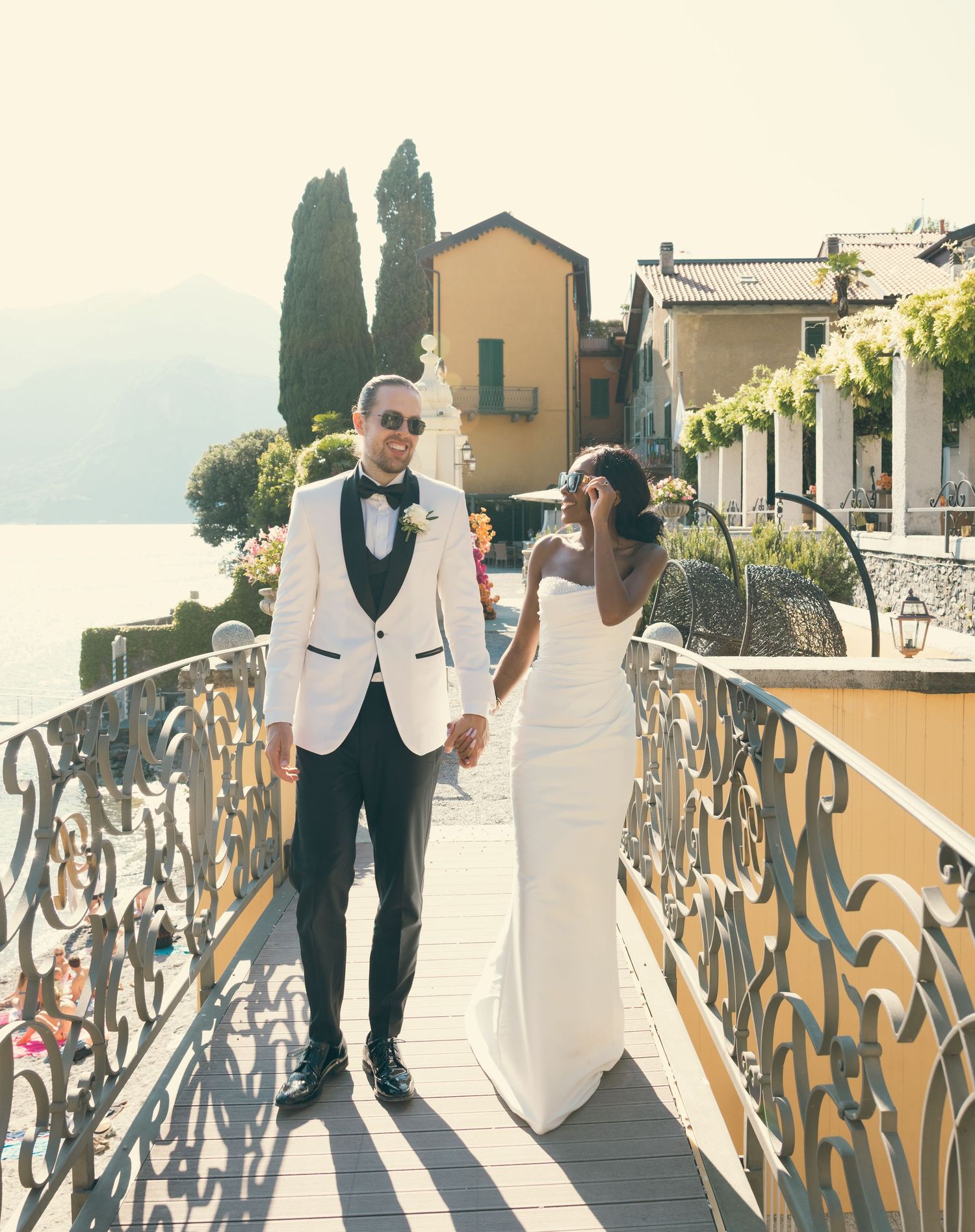 A couple in wedding attire walks along a scenic terrace overlooking Lake Como in Italy.