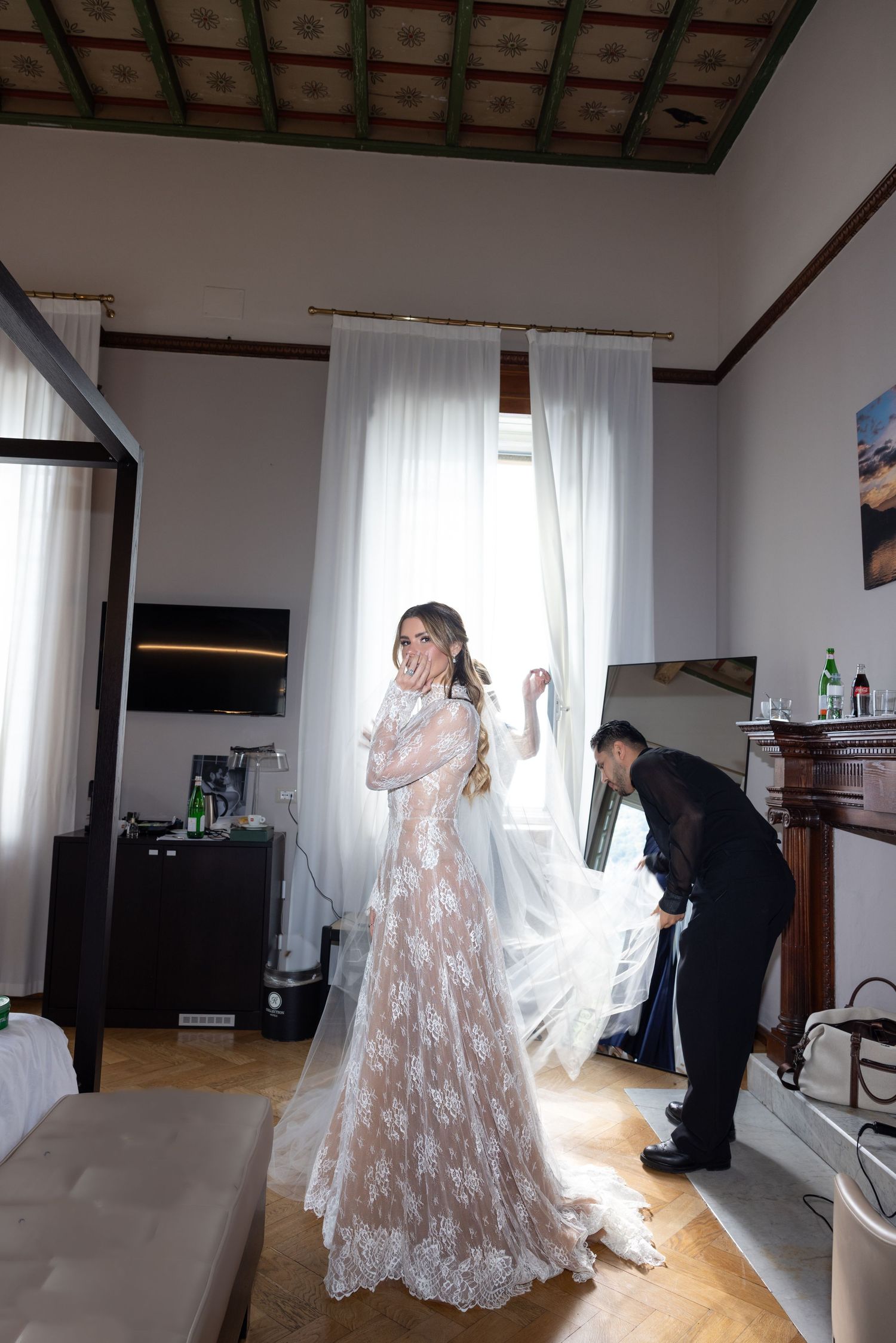 A wedding dress fitting session showing the delicate lace details and flowing train in a bright interior room.