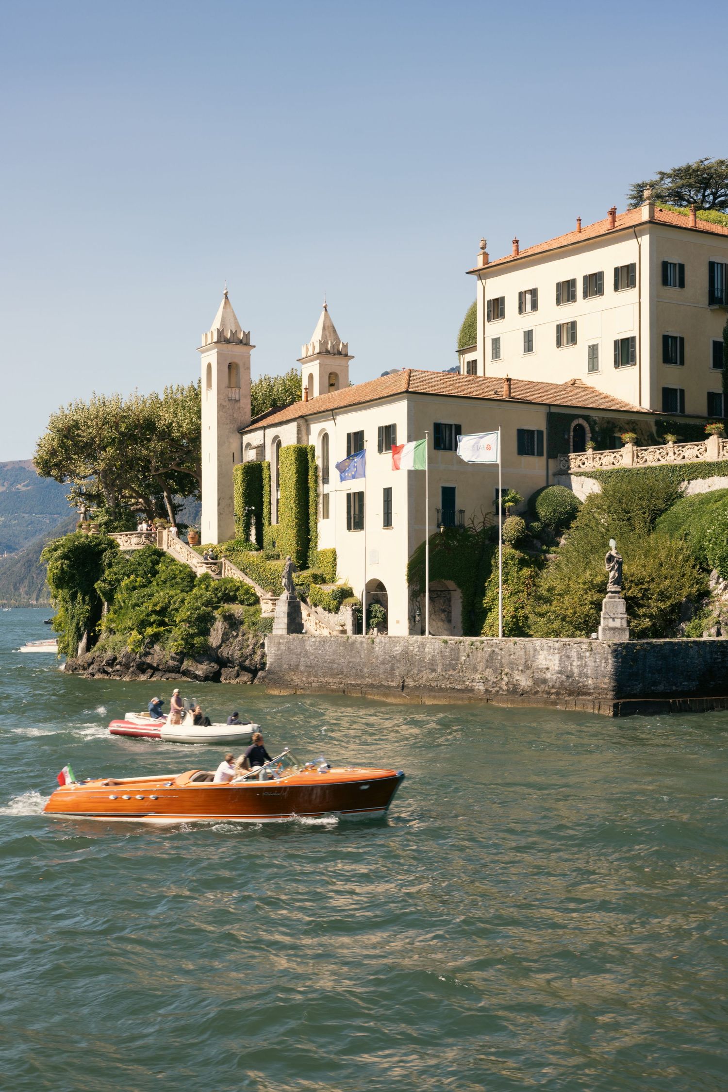 Classic Italian villa on Lake Como with boats passing by on turquoise waters.