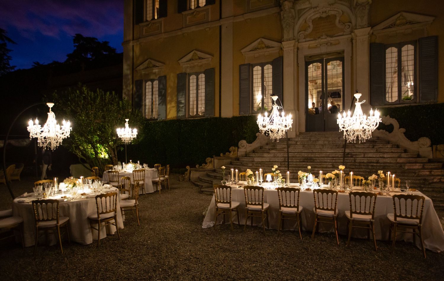 Evening wedding reception space illuminated by multiple hanging crystal chandeliers.