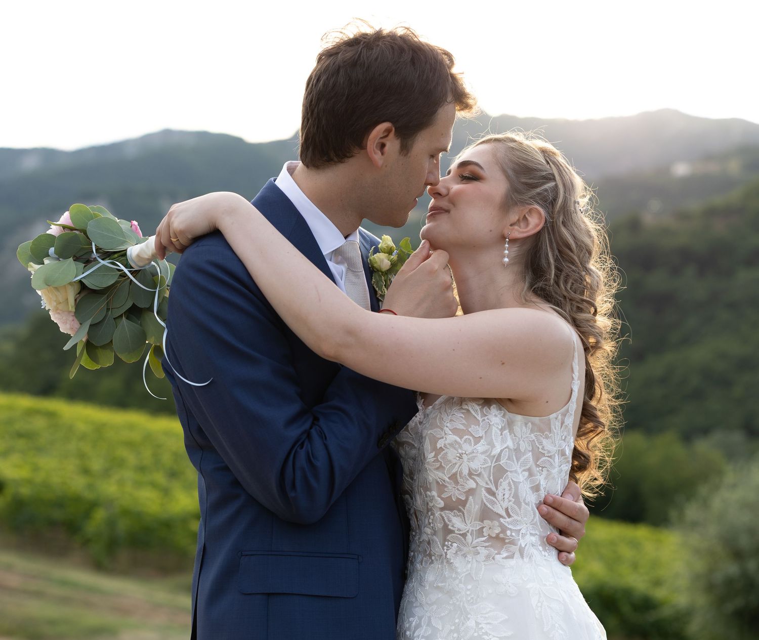 Wedding couple embraces passionately during outdoor photo session with mountain views.