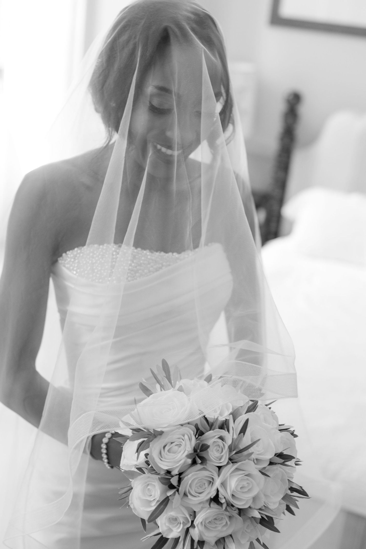 Bride in white wedding dress holding a beautiful bouquet of white roses with delicate veil detail.