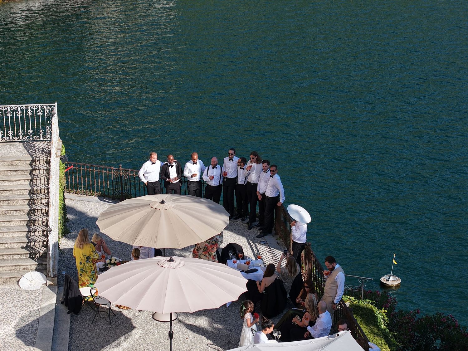 Wedding reception setup on a lakeside terrace with white umbrellas and mountain views.