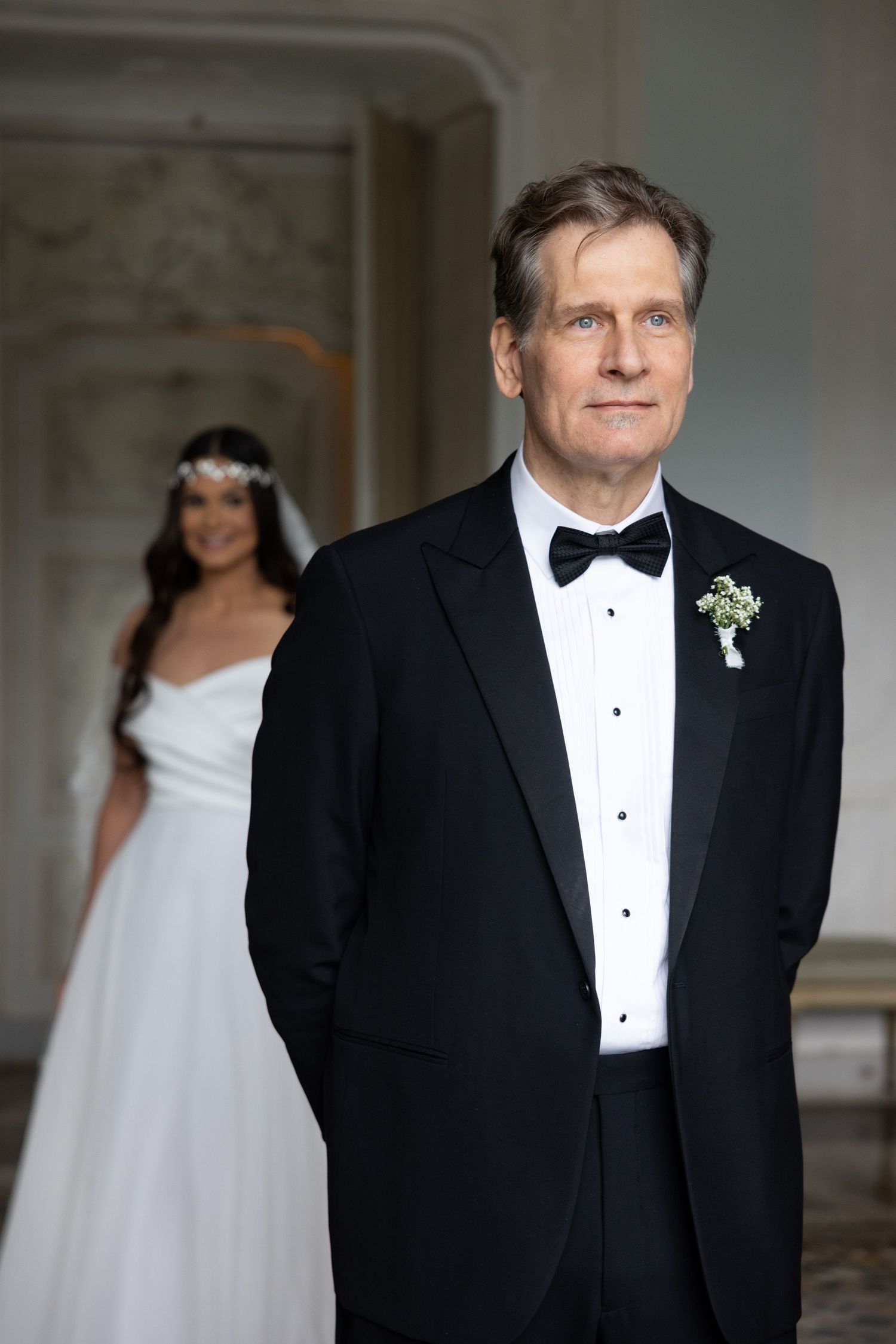 A wedding couple in formal attire poses in an elegant room with classical European architecture.