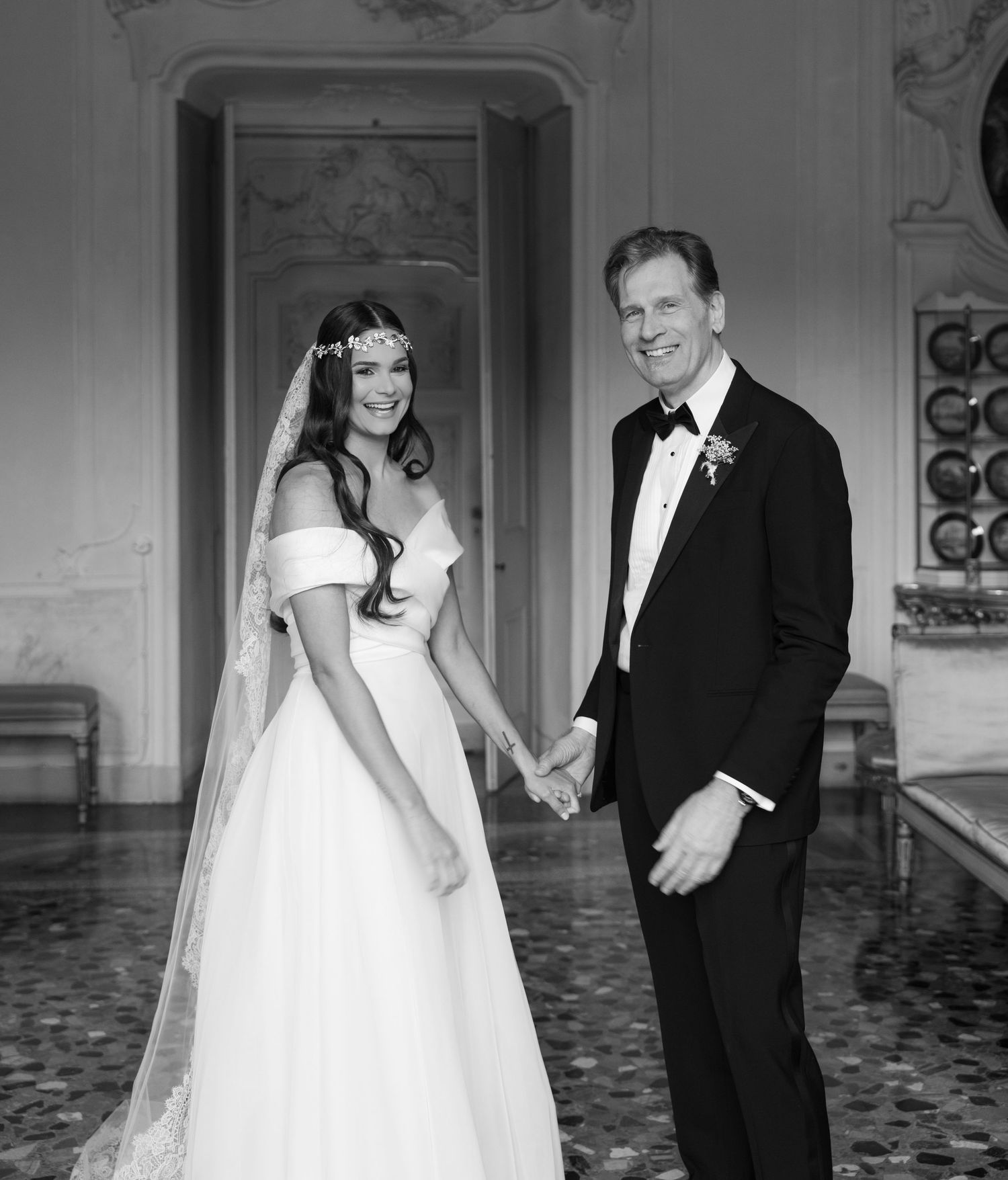 A wedding couple shares a candid moment in an elegant room with classical architecture and marble floors.