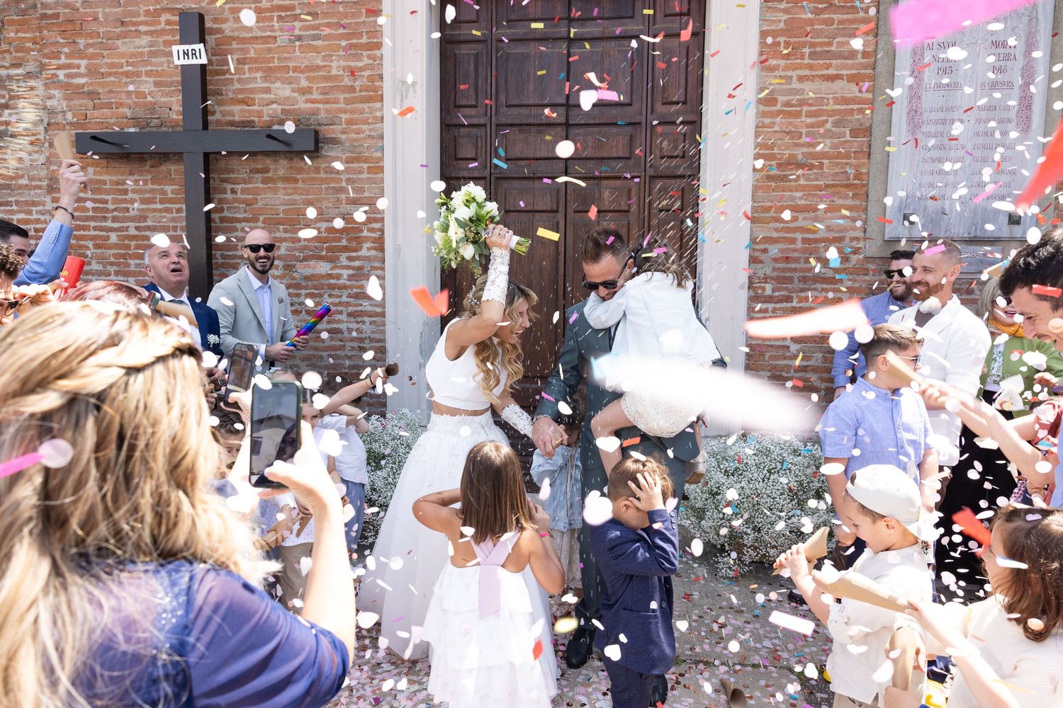 Wedding party and guests create a festive atmosphere with confetti outside a brick venue.