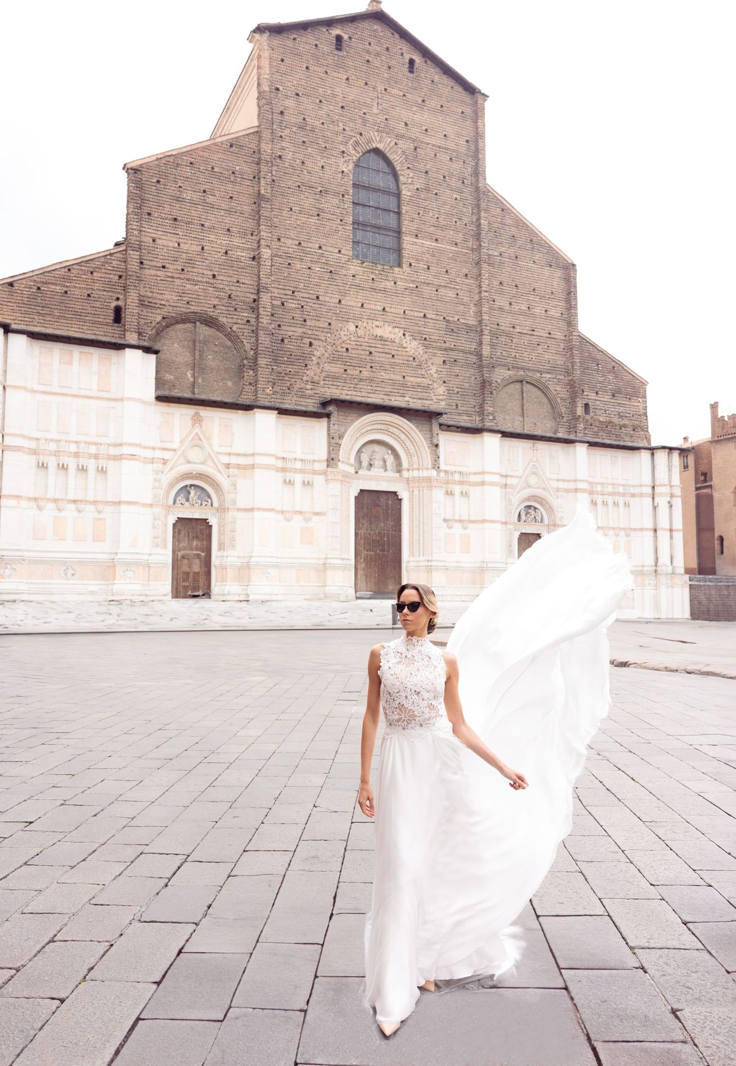 Elegant white wedding dress twirling in front of historic Italian church facade in Bologna.