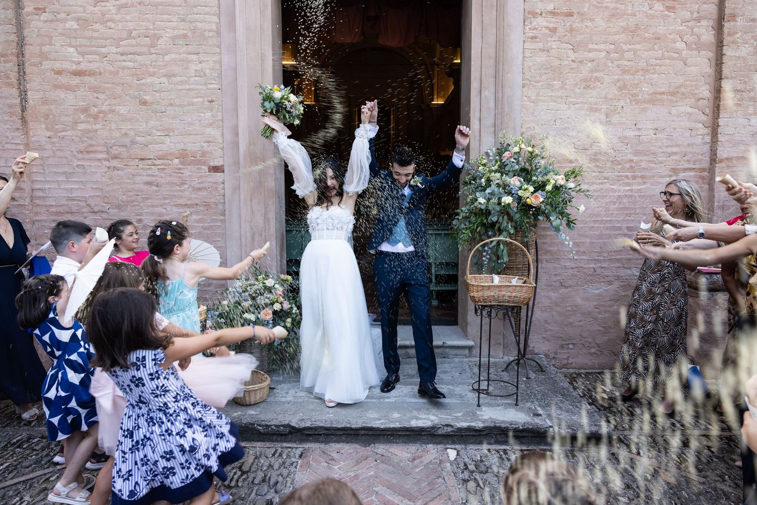 Wedding guests gather outside a brick church entrance with floral decorations.