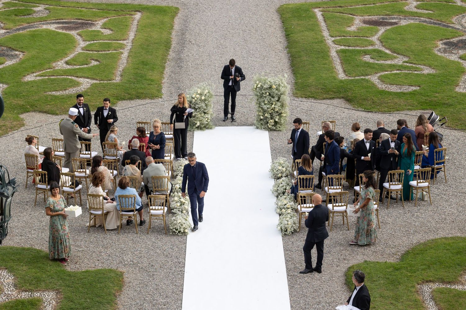Outdoor wedding ceremony setup with white chairs arranged on a gravel courtyard.