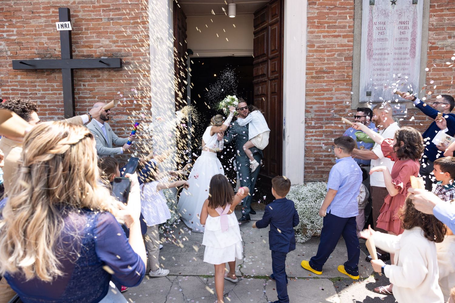 Wedding guests throw confetti outside a brick church entrance during a celebration.