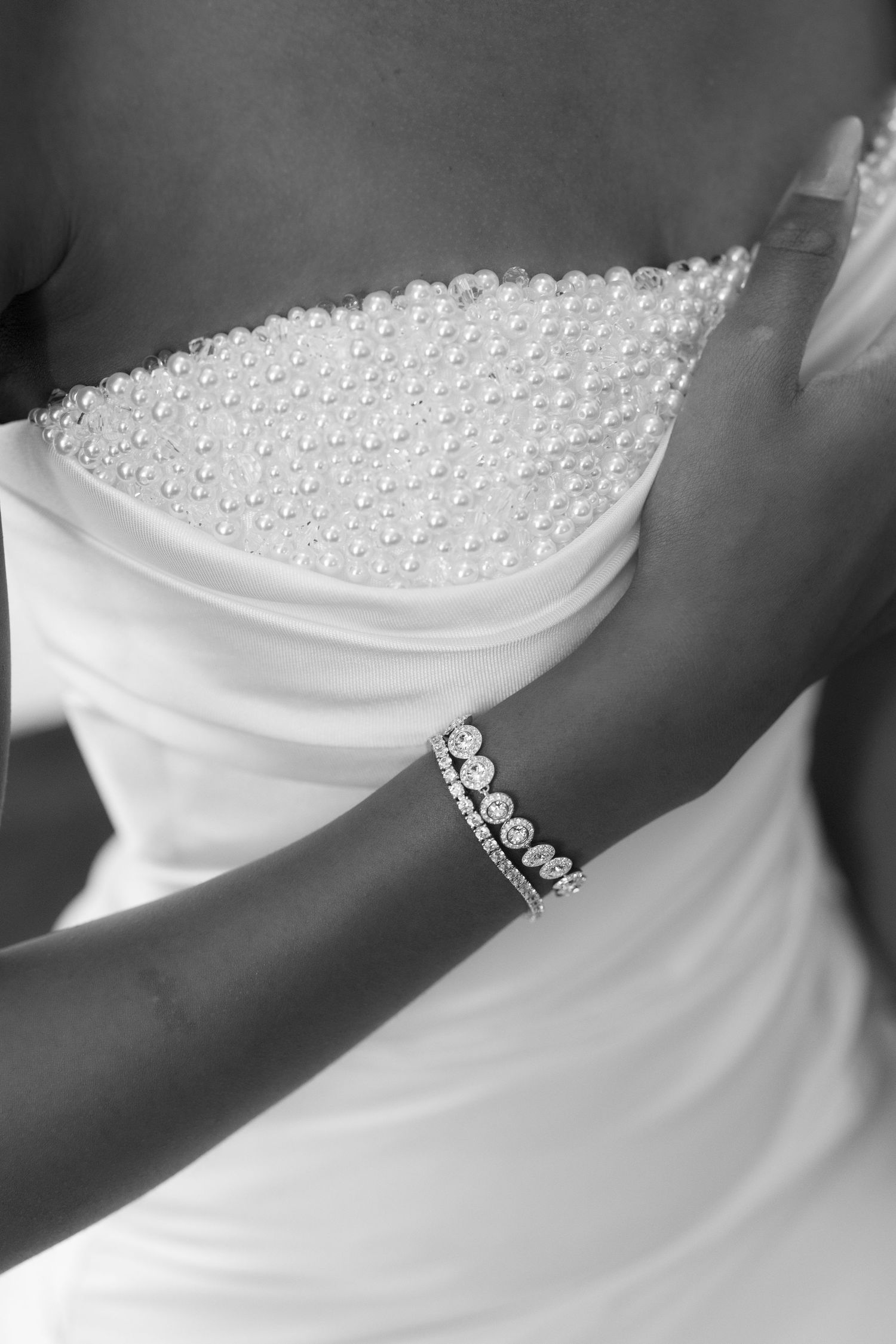 Close-up black and white photo of a pearl-beaded wedding dress bodice and diamond bracelet.