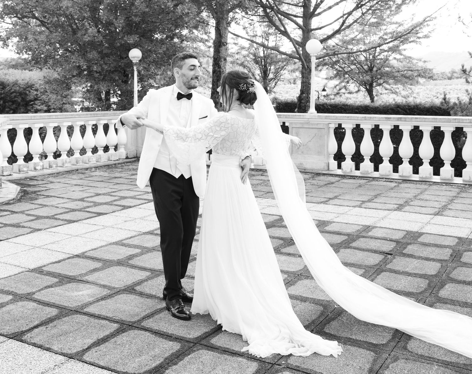 Wedding couple walking along a stone patio with white balustrades in the background.