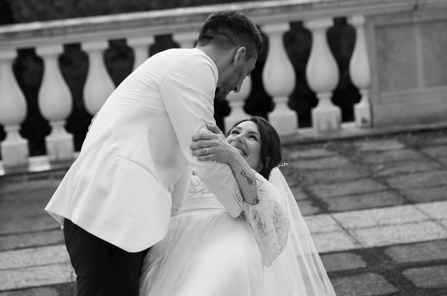 A romantic black and white wedding photo of a couple sharing an intimate moment on stone steps.