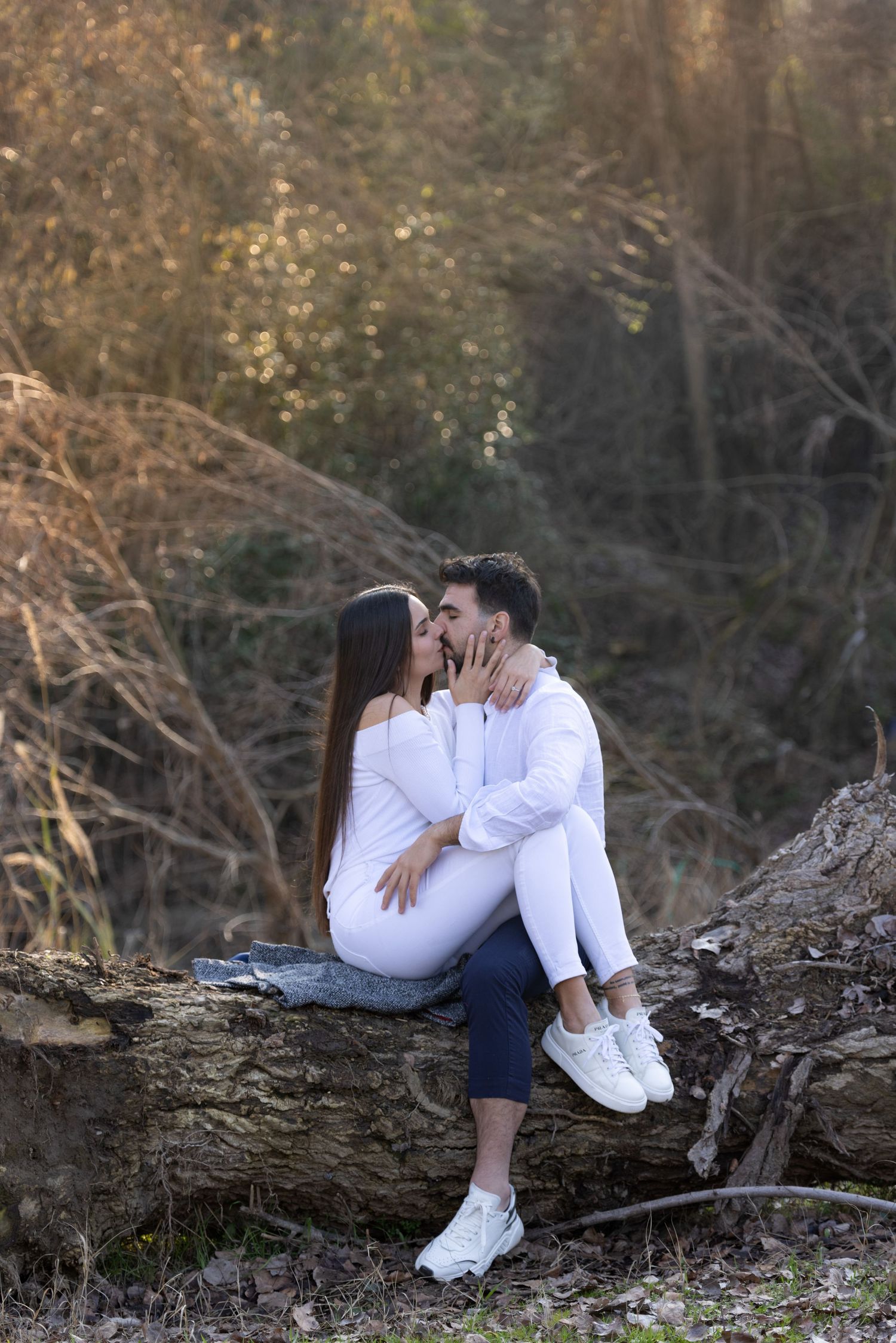 Couple sharing intimate moments while sitting on a fallen log in an autumn forest setting.