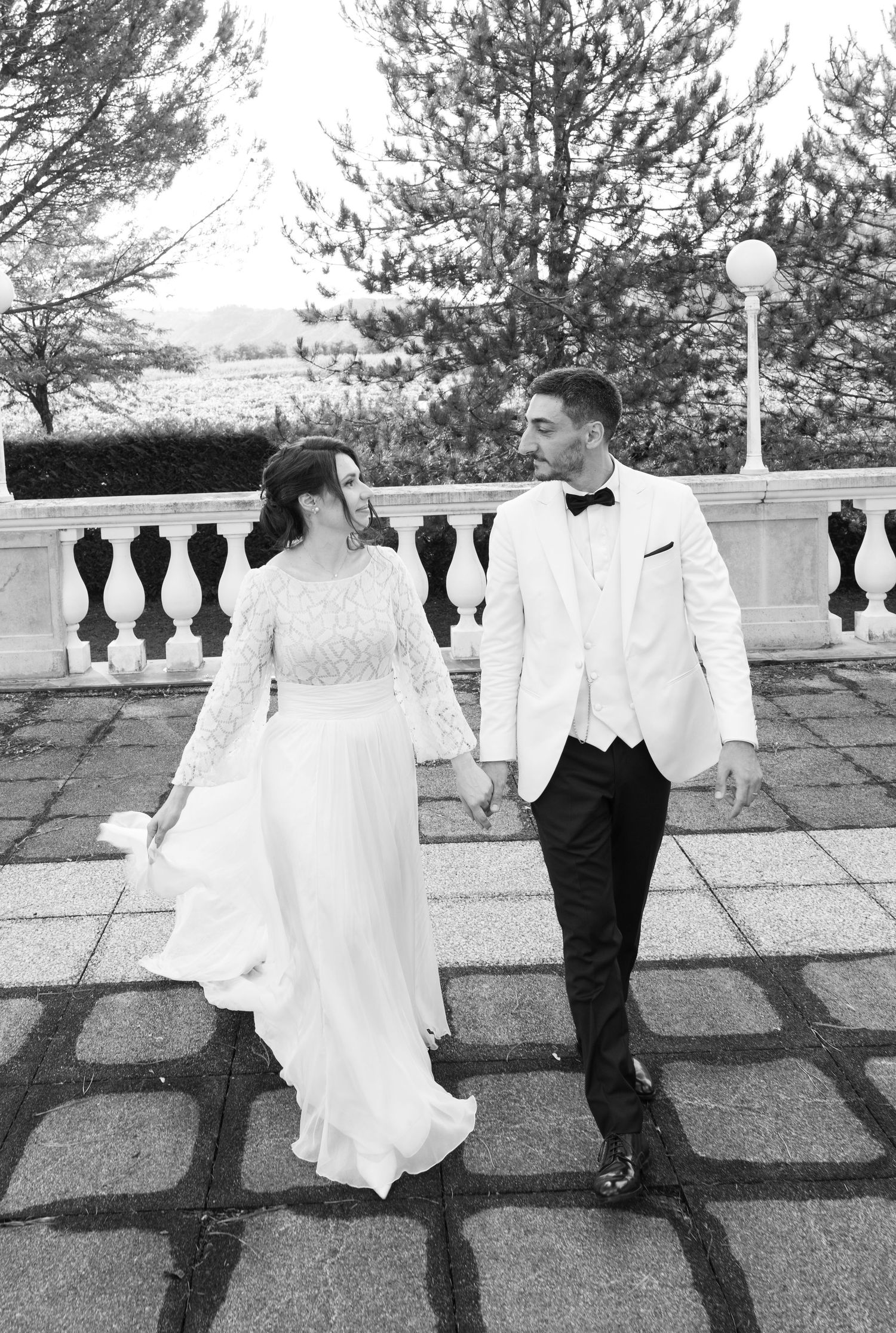 Black and white portrait of newlyweds walking together on stone terrace.
