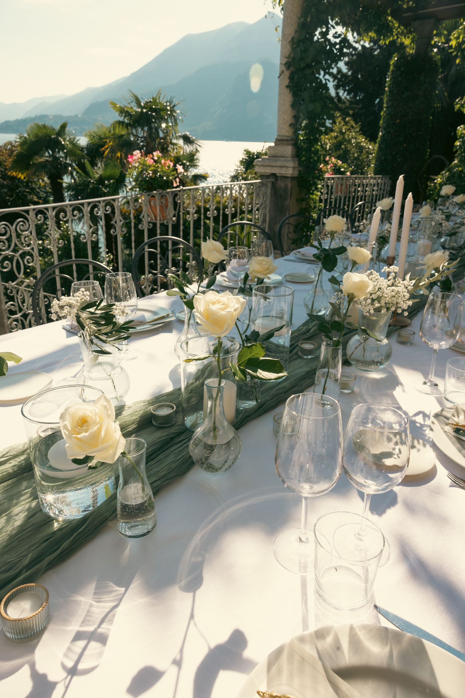 Elegant outdoor wedding table setting on a terrace overlooking Lake Como with white roses and mountain views.