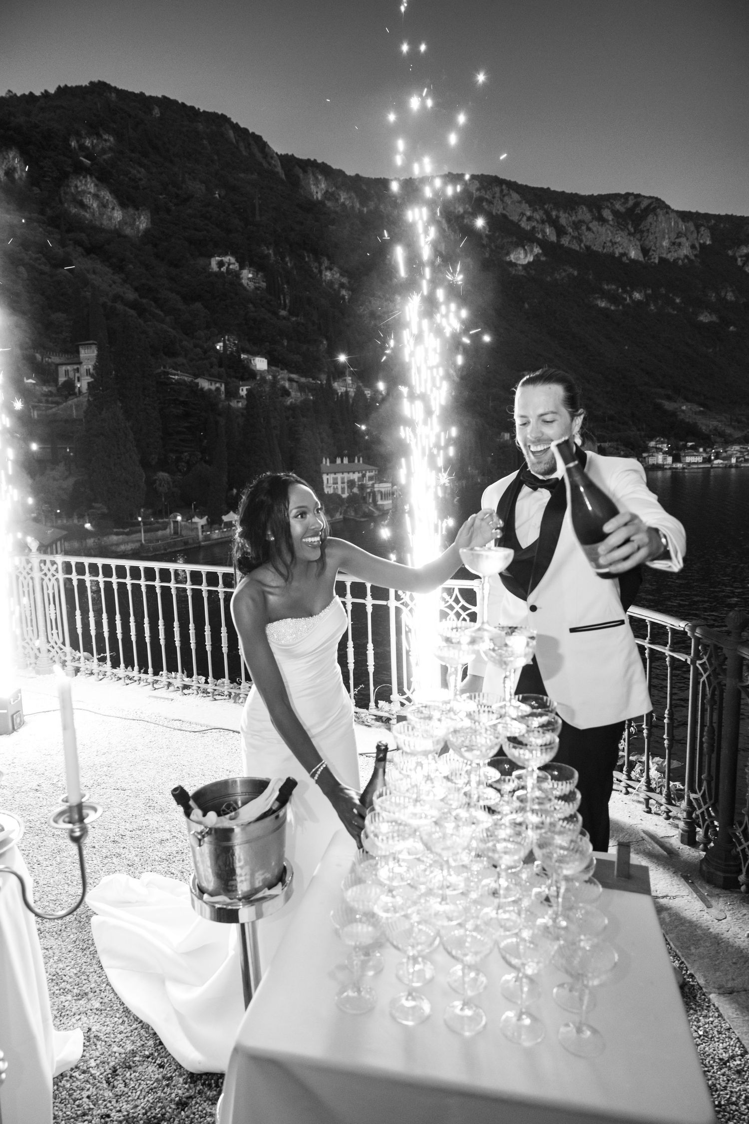 A sequence of black and white photos showing a couple reacting excitedly to sparklers on a balcony overlooking mountains.