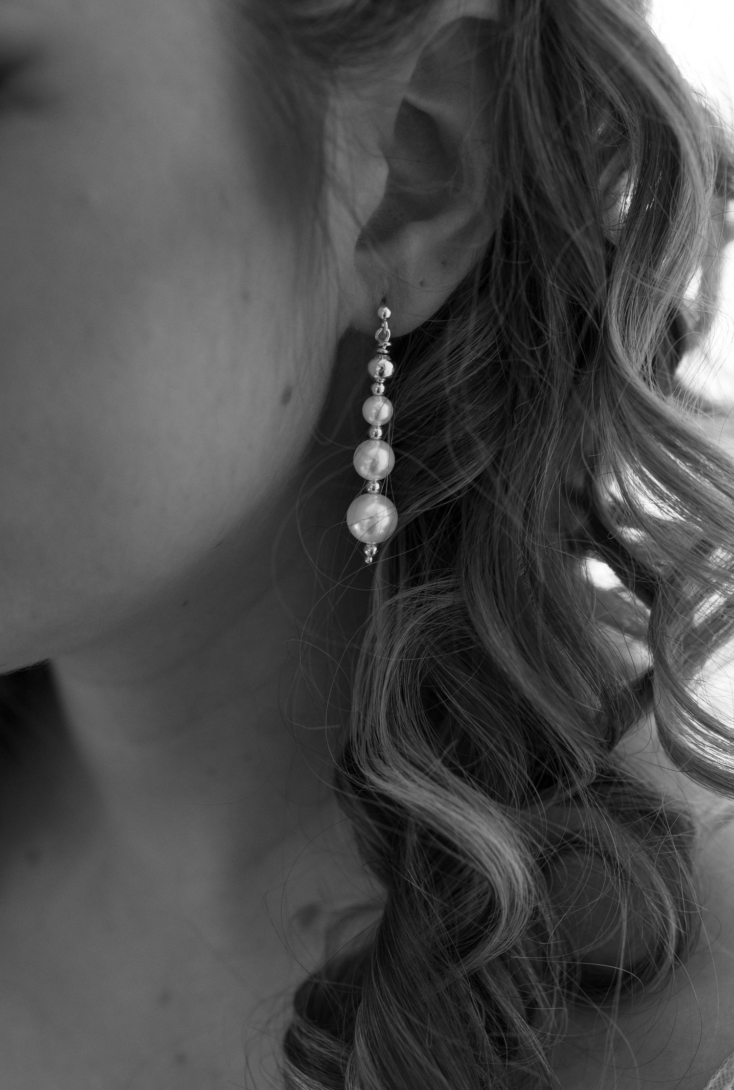 Close-up of pearl drop earrings with curled hair in black and white.