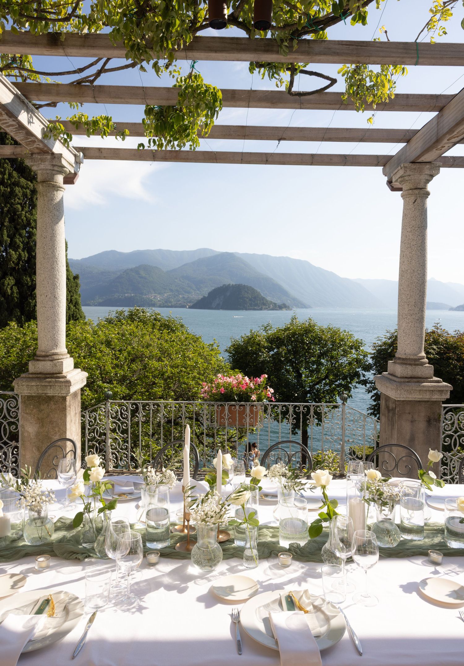 Elegant outdoor wedding reception tables set under a pergola with stunning ocean and mountain views in the background.