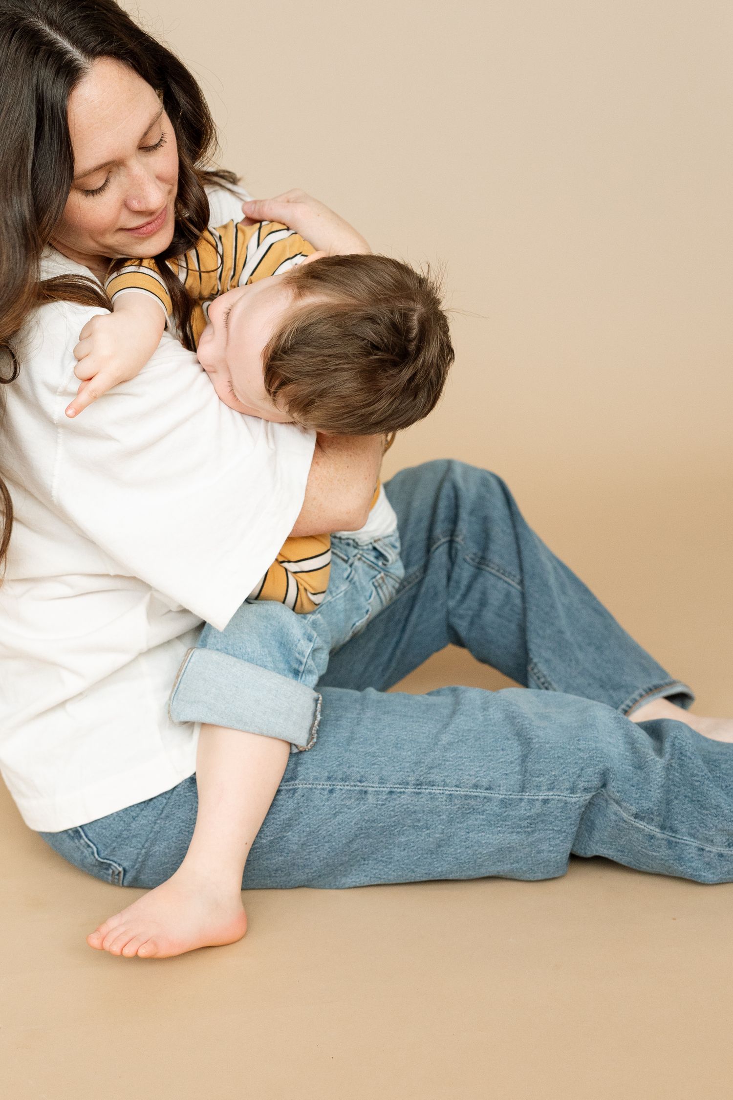 A person in a white top and blue jeans lying down and looking at something in a casual, relaxed pose against beige background.