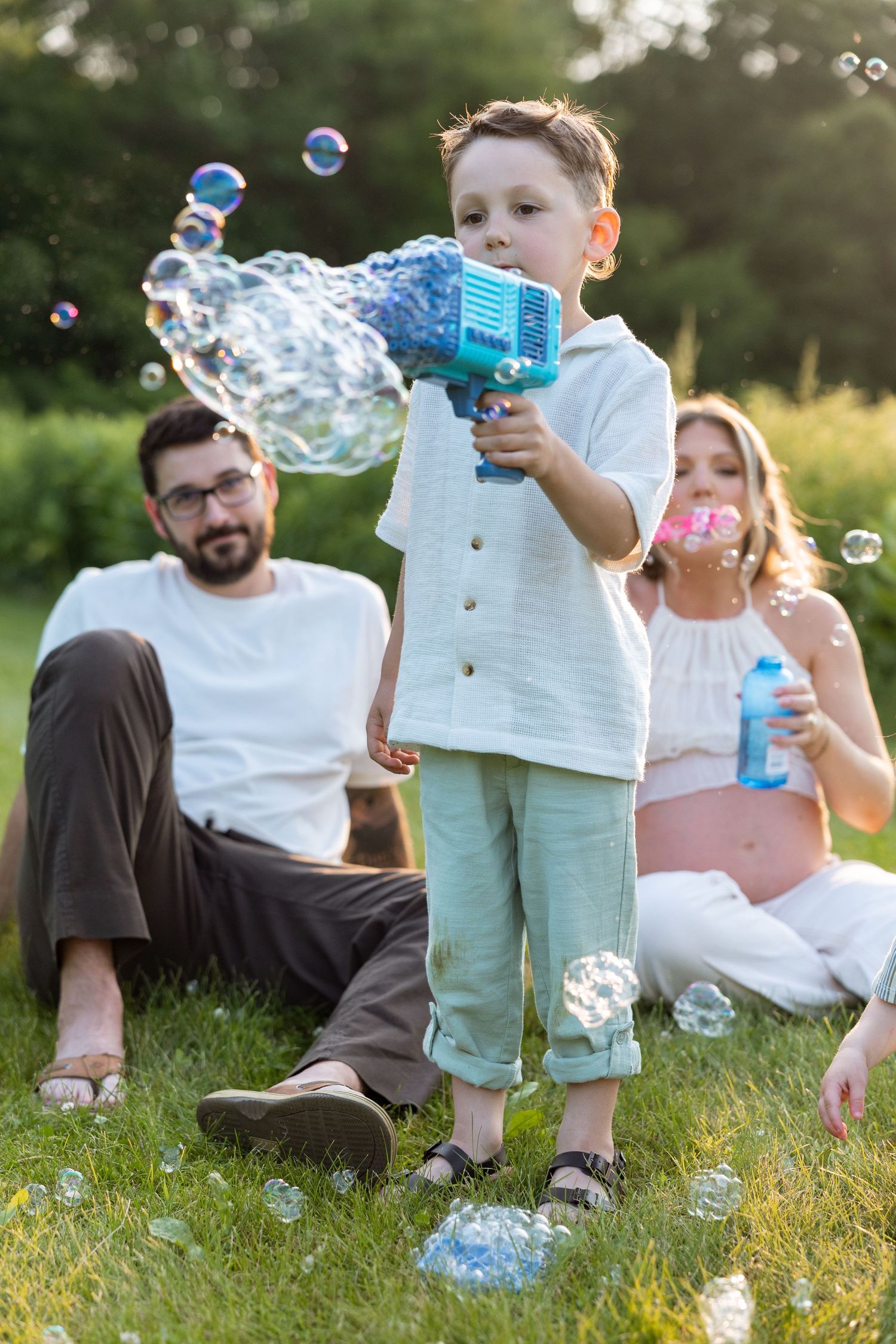 Family playing with soap bubbles on grass in summer evening light.