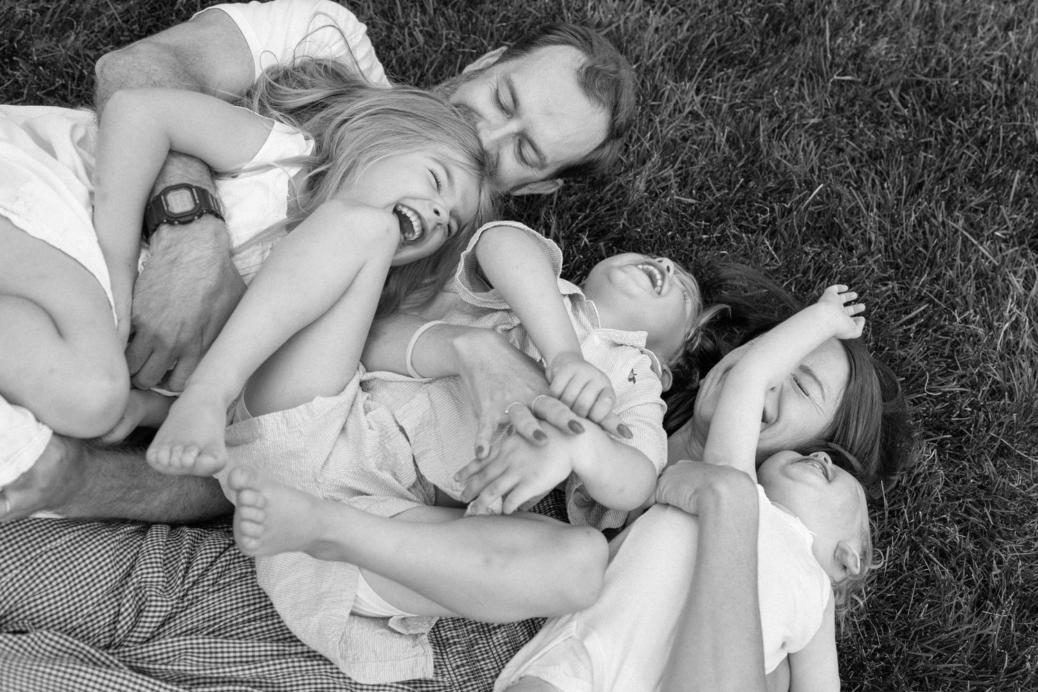 A family relaxes together on a picnic blanket in the grass on a sunny afternoon.