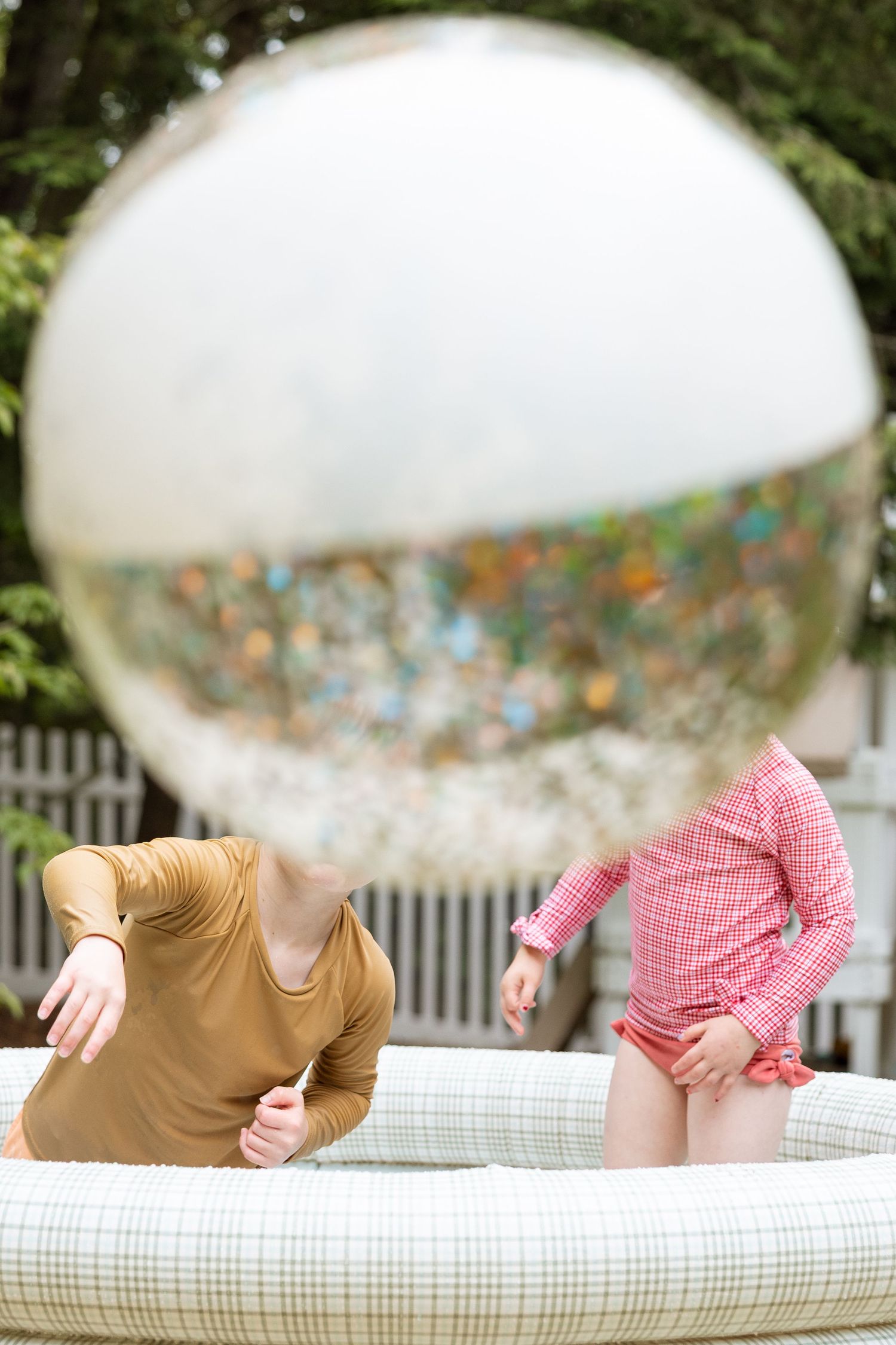 Two people lean over a white inflatable pool with a large festive balloon floating above them.