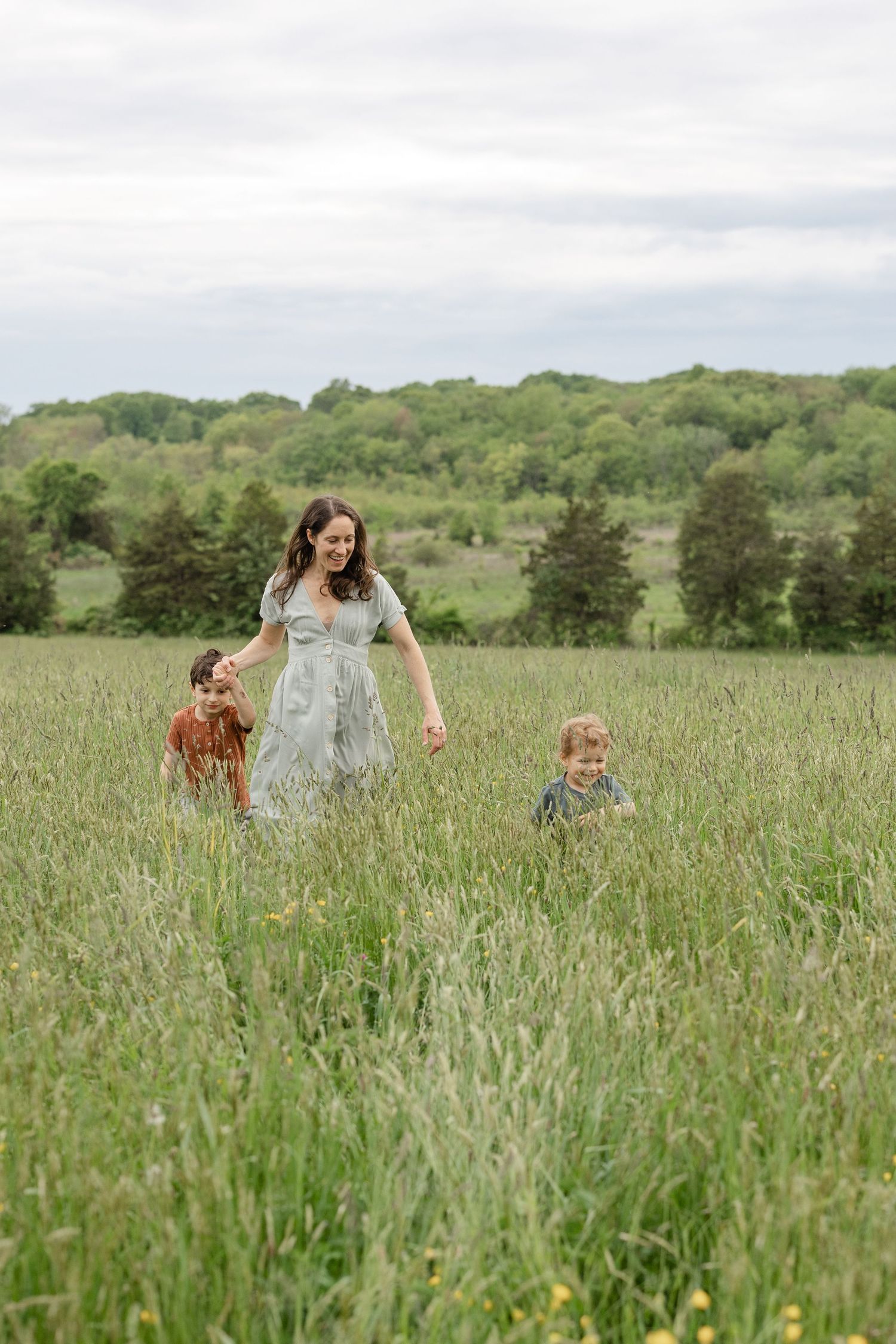 People and their dog explore a lush green meadow on a bright summer day with rolling hills in the background.