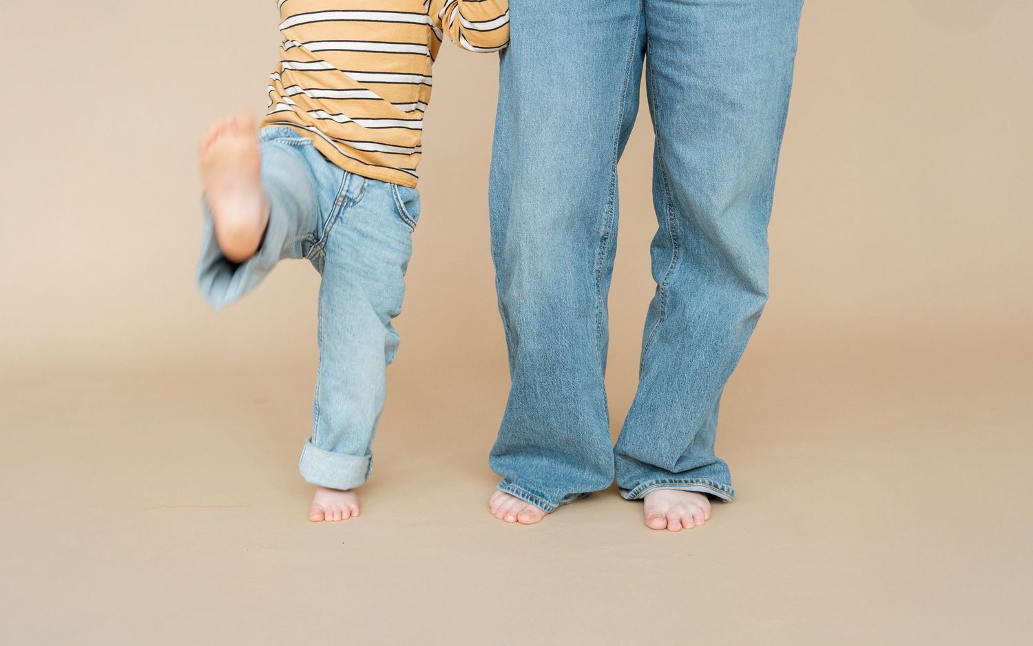 Baby feet and parent feet are lovingly posed together on neutral beige background.