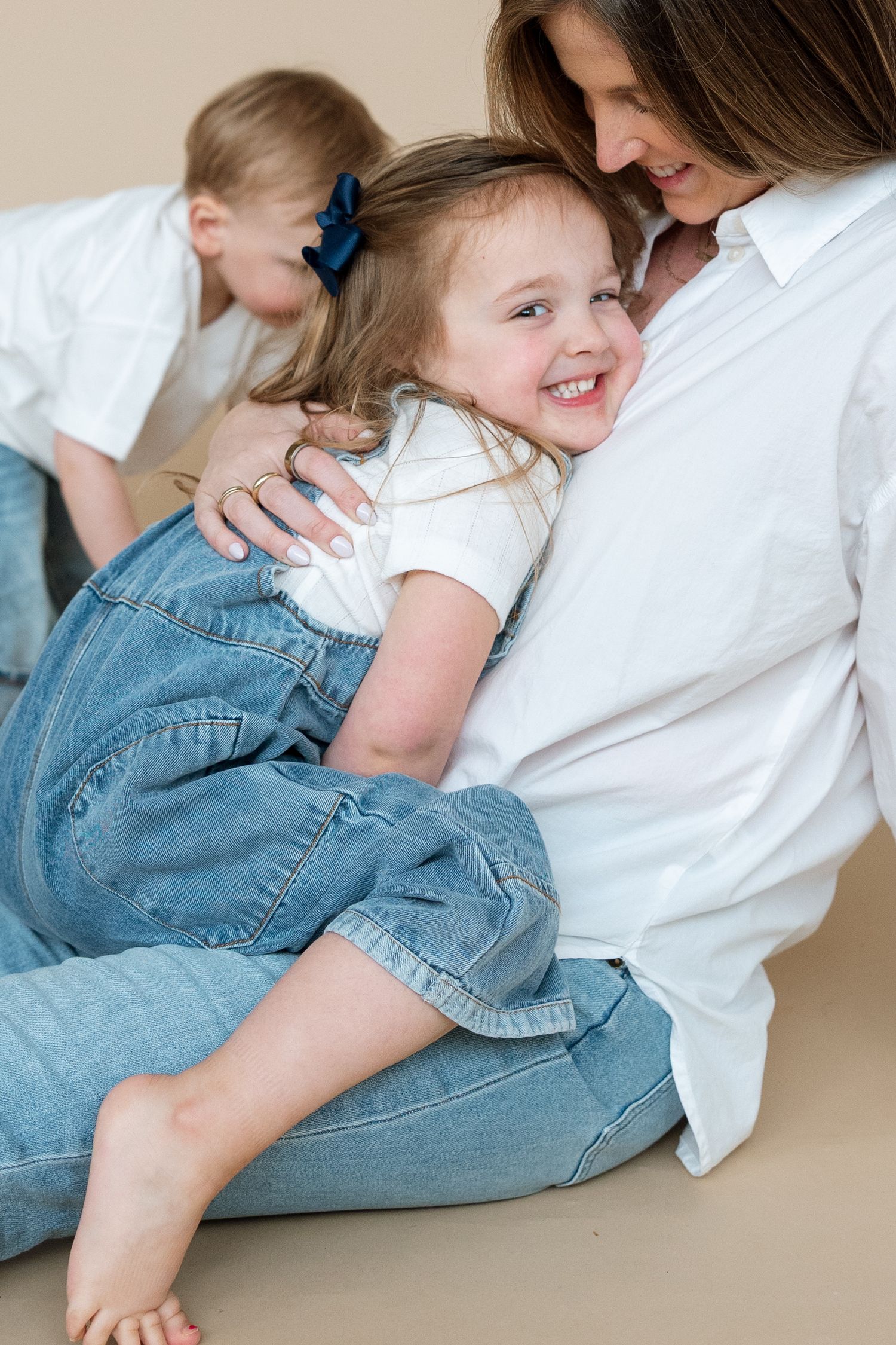 A child in denim overalls and white shirt plays and laughs on a neutral-colored floor in a sequence of candid shots.